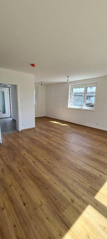 Großes, leeres Wohnzimmer mit Holzboden und mehreren Fenstern, die viel Tageslicht hereinlassen.