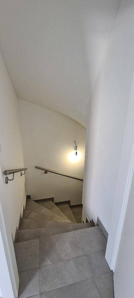 Treppenhaus mit grauen Fliesenstufen und einem Handlauf, das die verschiedenen Etagen verbindet.