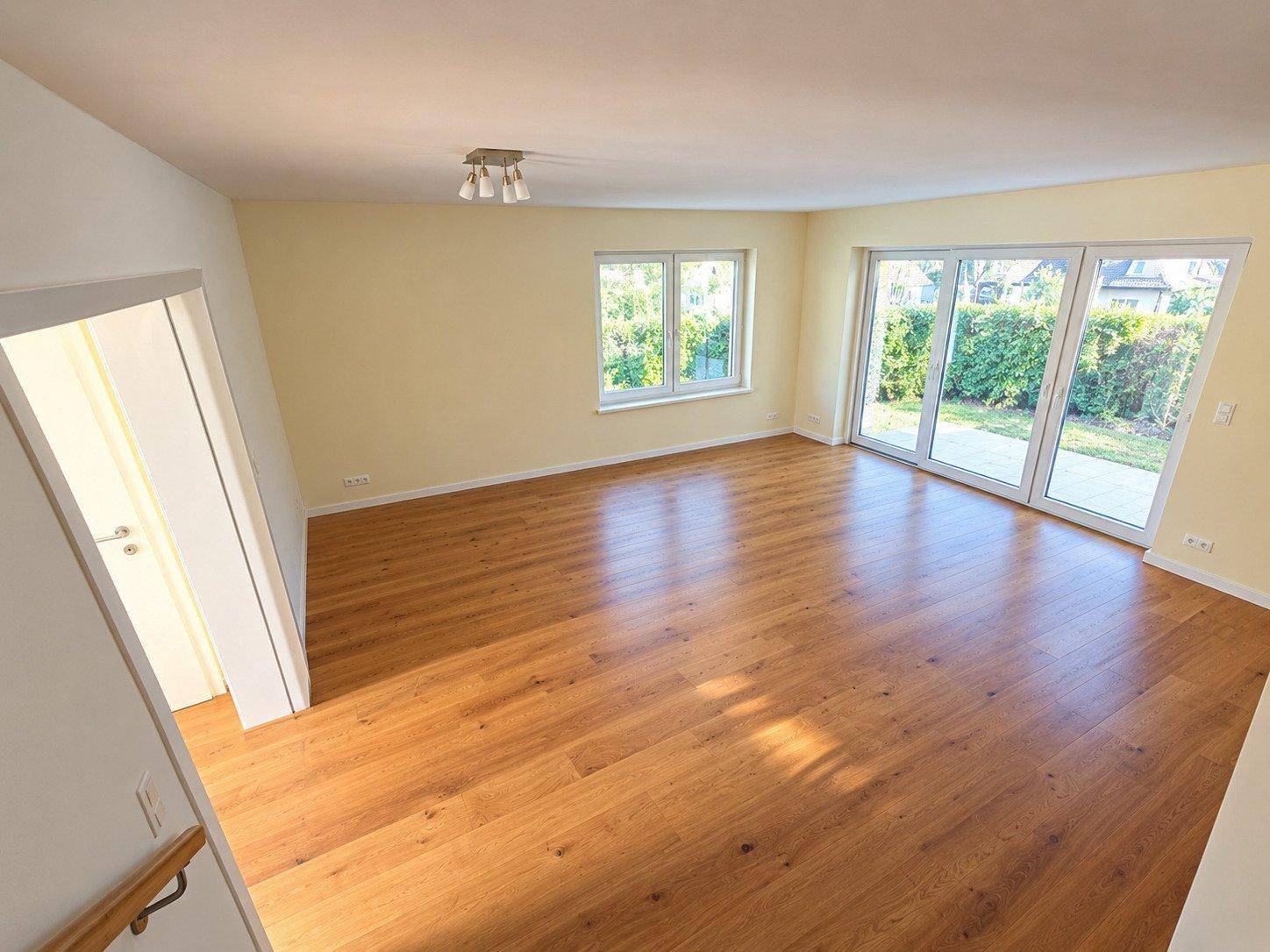 Helles Wohnzimmer mit hochwertigem Parkettboden und großen Fenstern mit Zugang zum Garten.