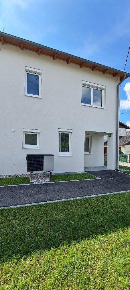 Rückansicht des Hauses mit Wärmepumpe und gepflegtem Rasen unter strahlendem Himmel.