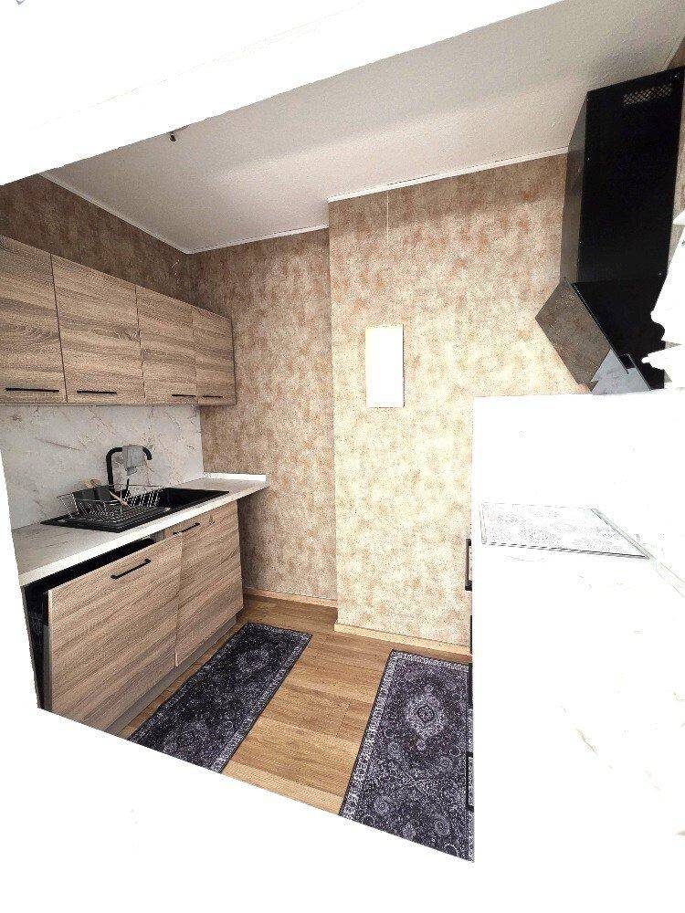 Moderne Küchenzeile mit Holzschränken, dunkler Spüle und einer Dunstabzugshaube.