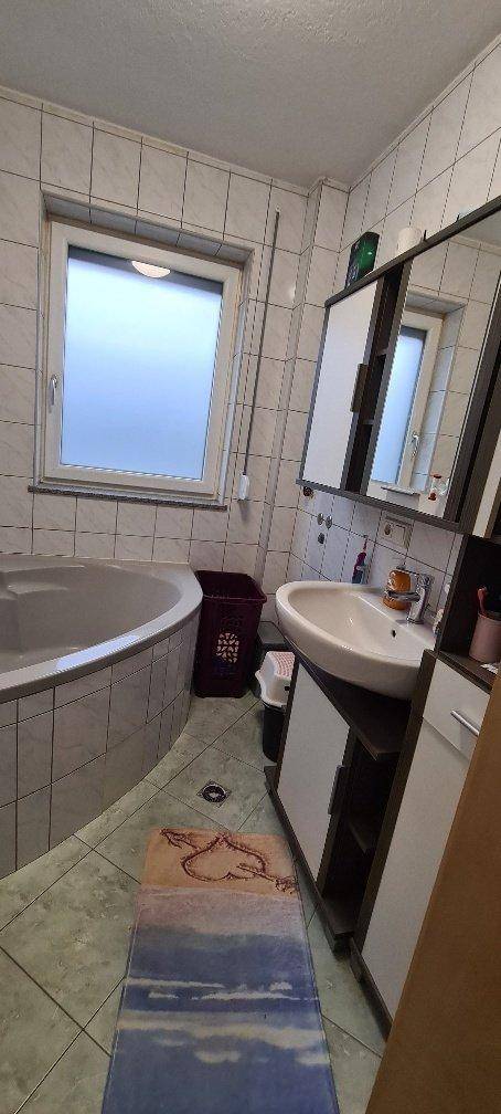 Badezimmer mit Eckbadewanne, Fenster und modernem Waschtisch.