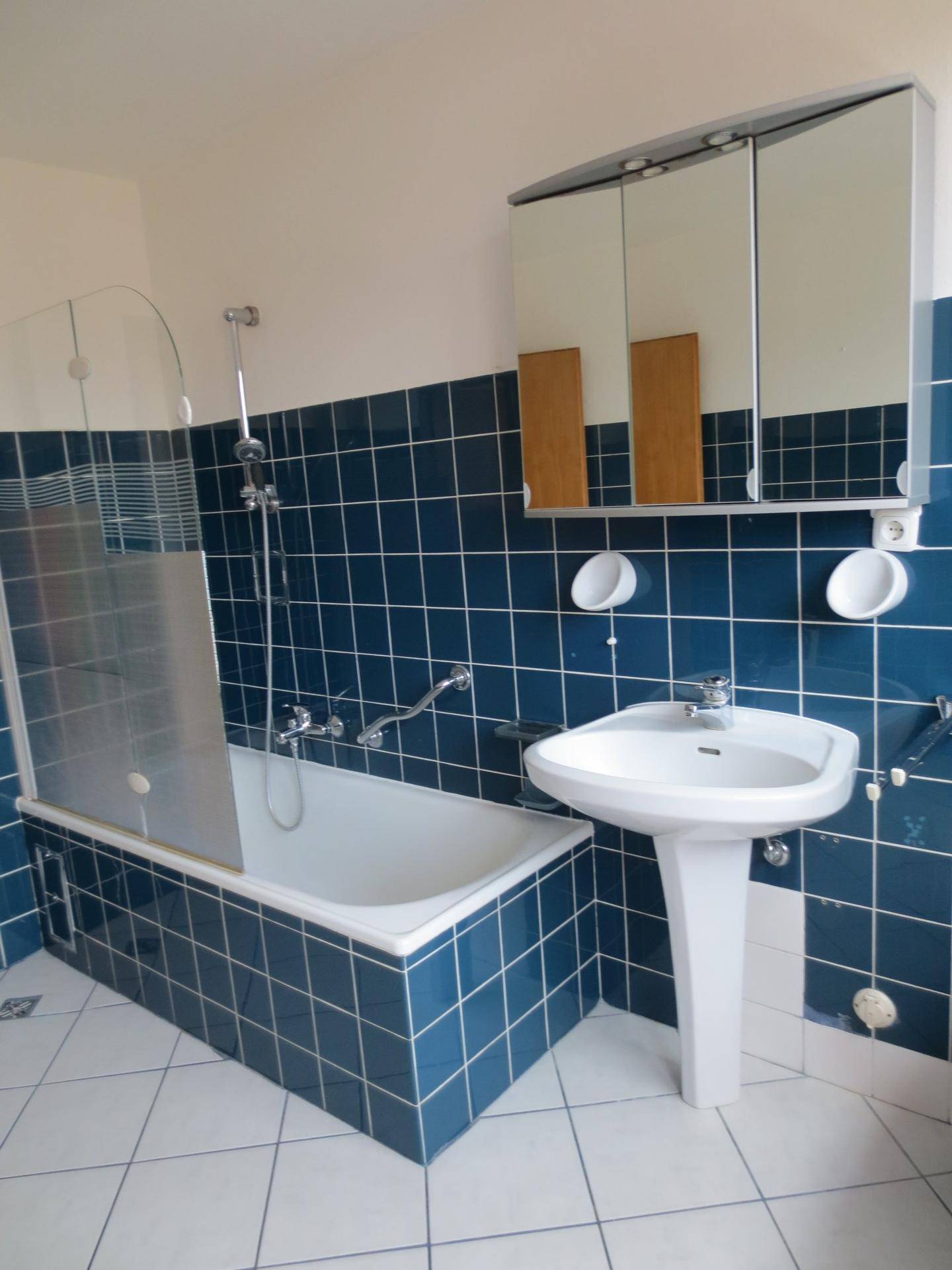 Badezimmer mit blauen Fliesen, Badewanne mit Duschfunktion und Spiegelschrank.