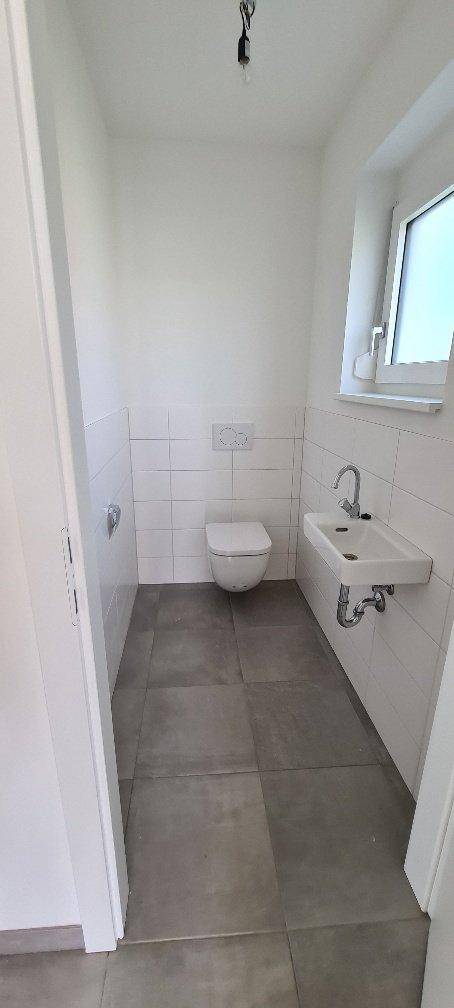 Modernes Gäste-WC mit wandhängender Toilette, kleinem Waschbecken und Fenster für Tageslicht.