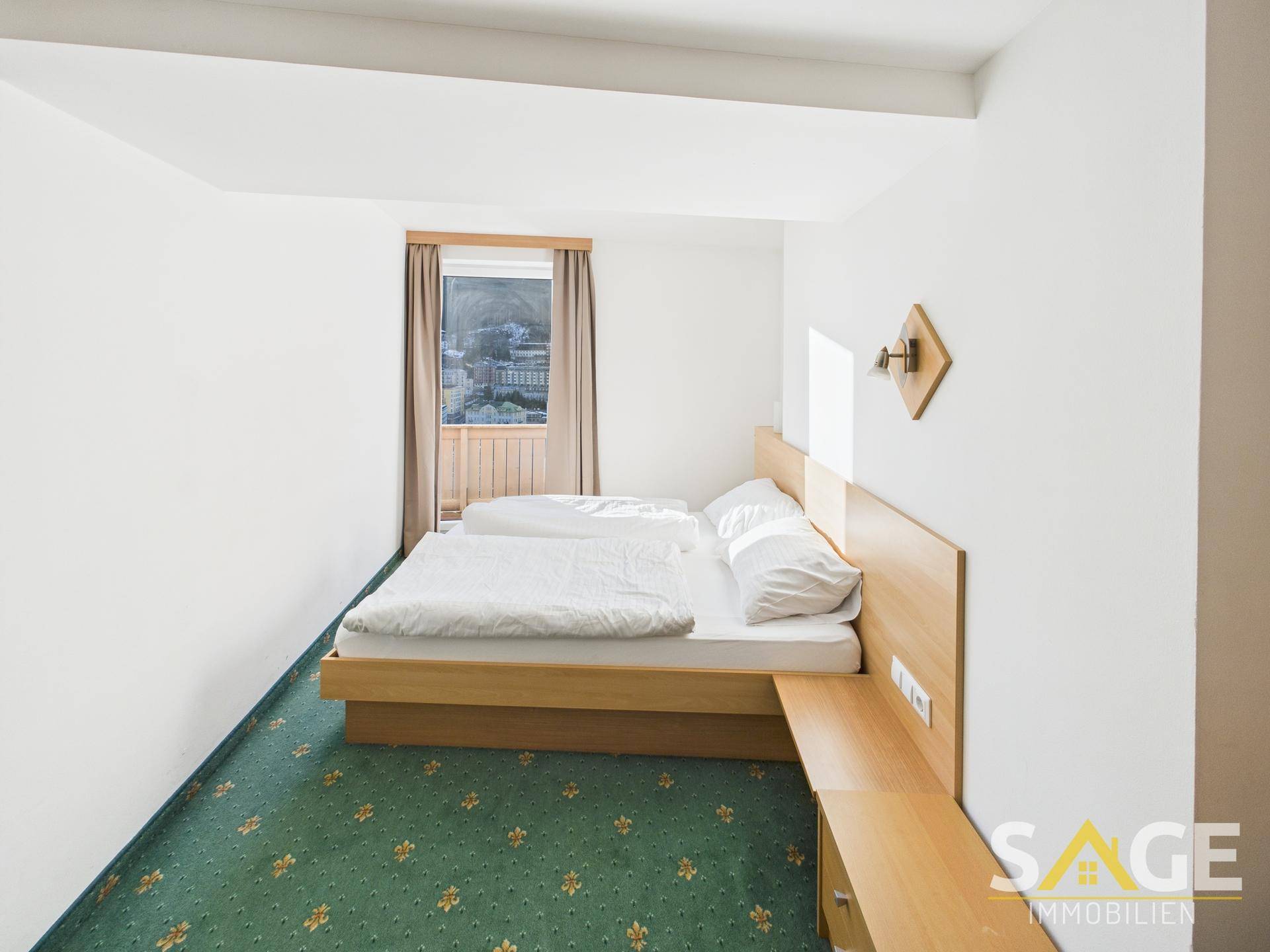 Helles Schlafzimmer mit zwei Einzelbetten, Teppichboden und Fenster mit Blick auf die Stadt.