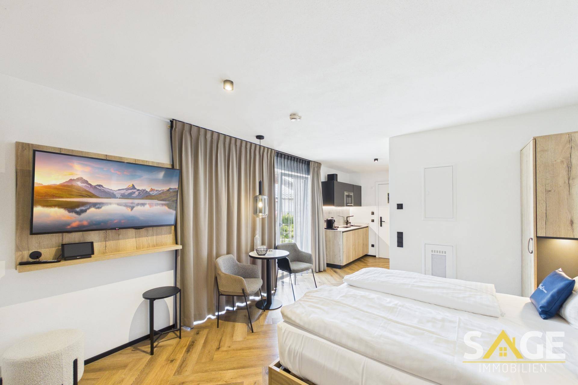 Modernes Schlafzimmer mit integrierter Küchenzeile, Fernseher und Holzboden, ideal für ein Studio-Apartment.