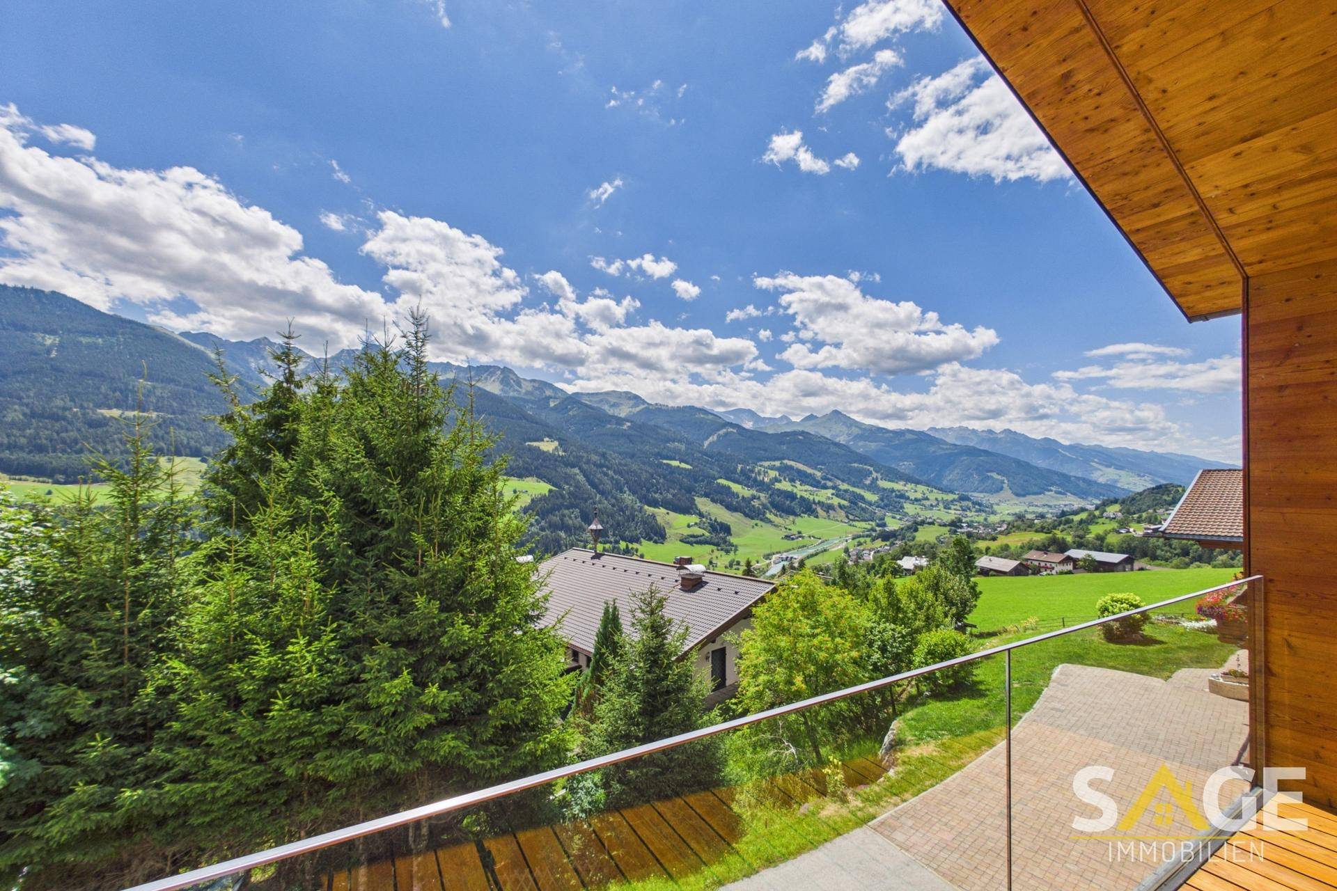 Panoramablick vom Balkon auf die umliegende Berglandschaft und grüne Täler mit vereinzelten Häusern.