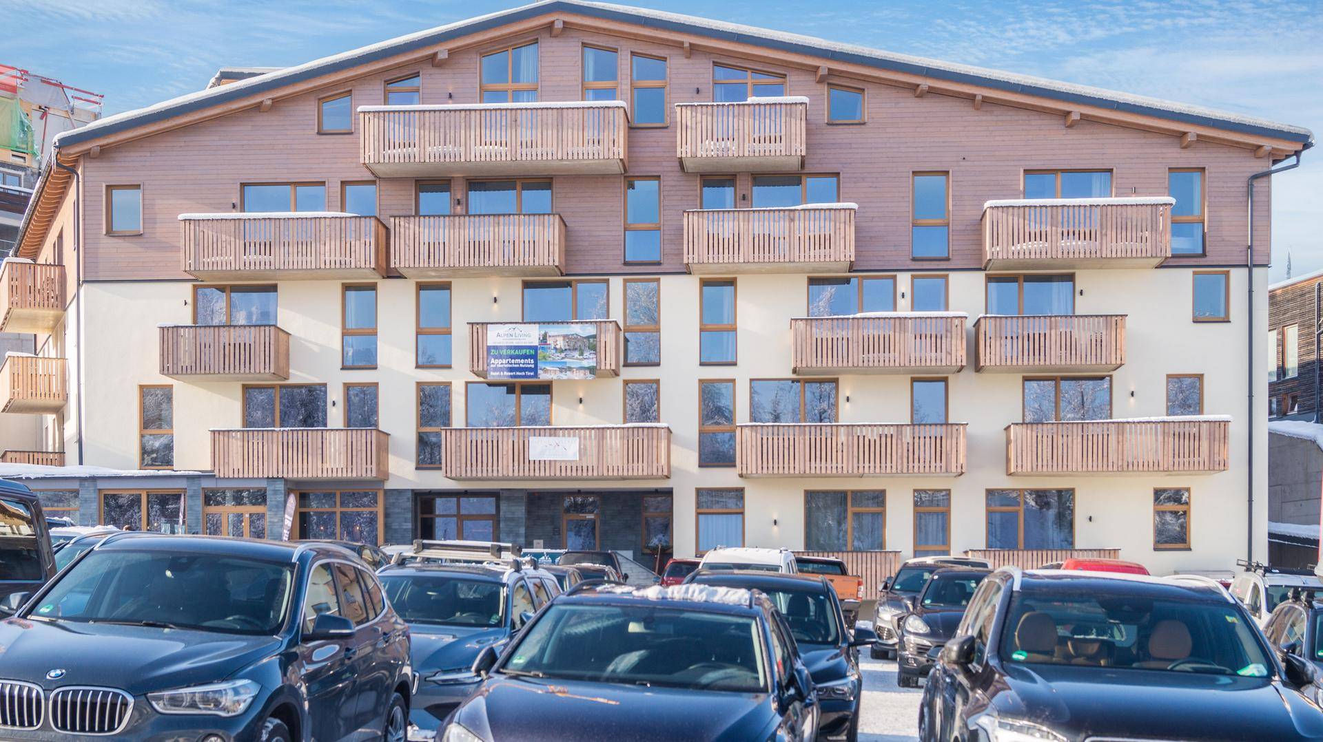 Moderne Gebäudefassade mit zahlreichen Balkonen und Holzverkleidung in winterlicher Umgebung.