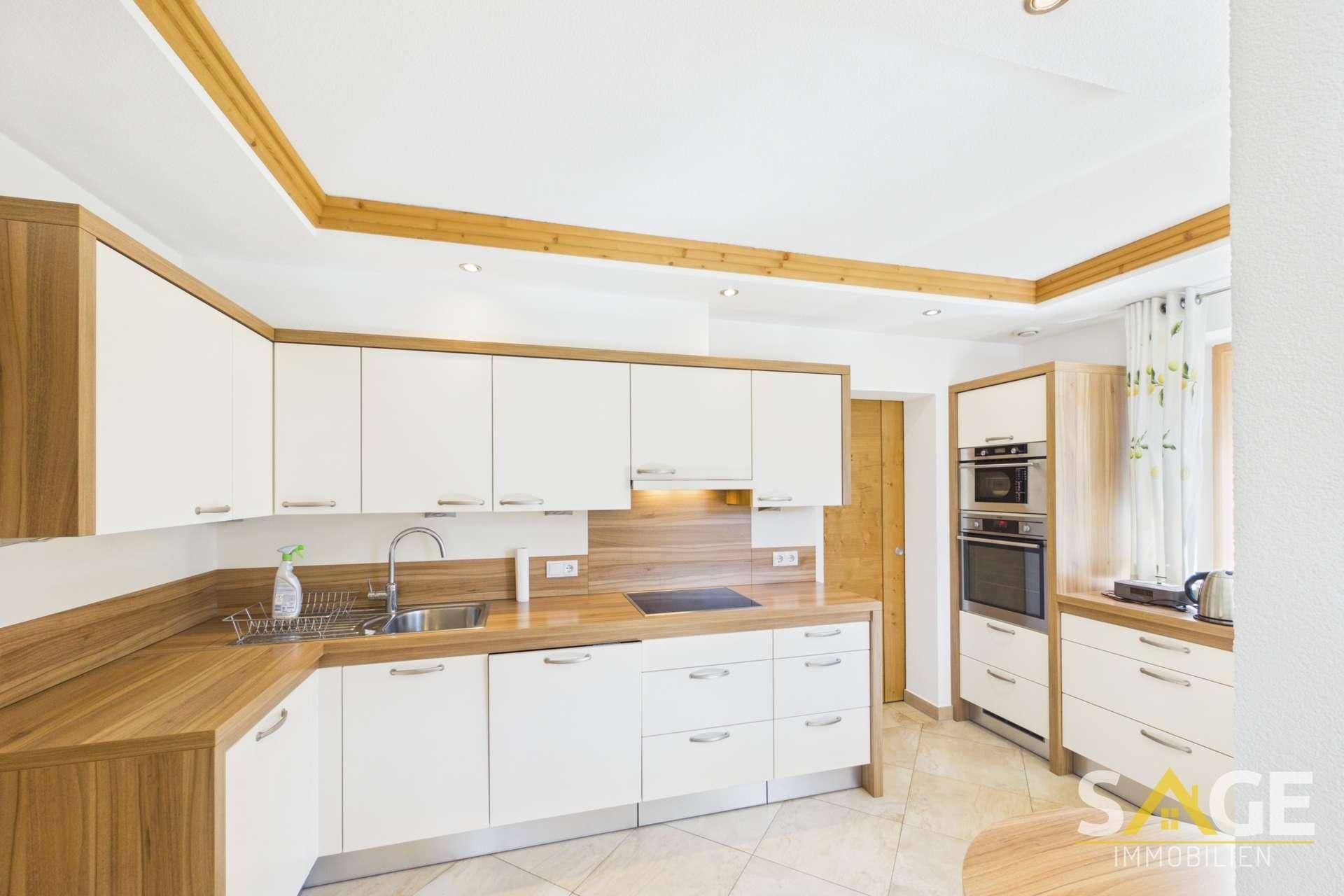 Moderne Küche mit weißen und holzfarbenen Schränken, integrierten Geräten und Fliesenboden.