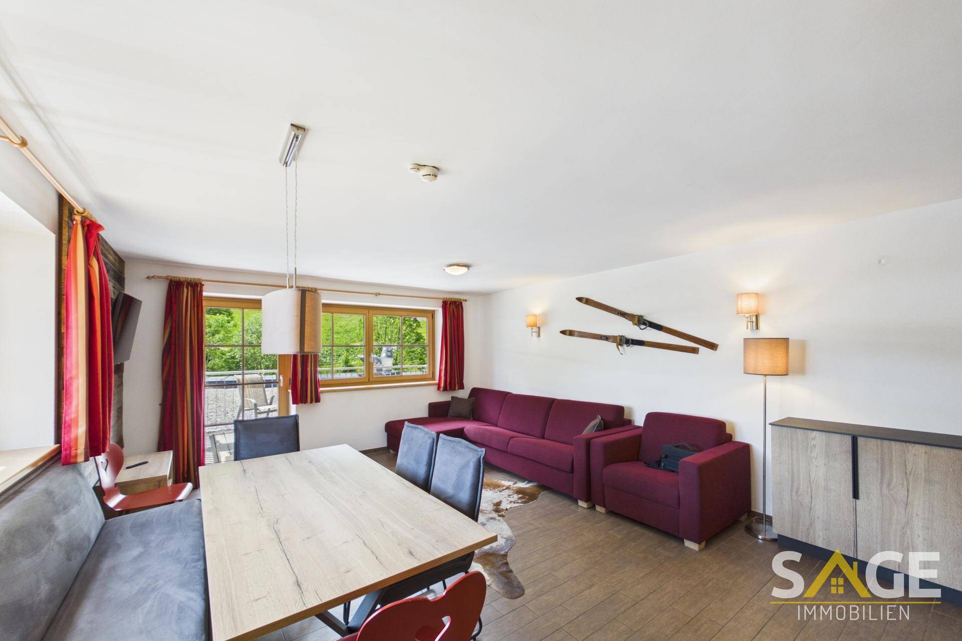 Gemütlicher Wohn- und Essbereich mit Holztisch, Sitzbank und roten Sofas im alpinen Stil.