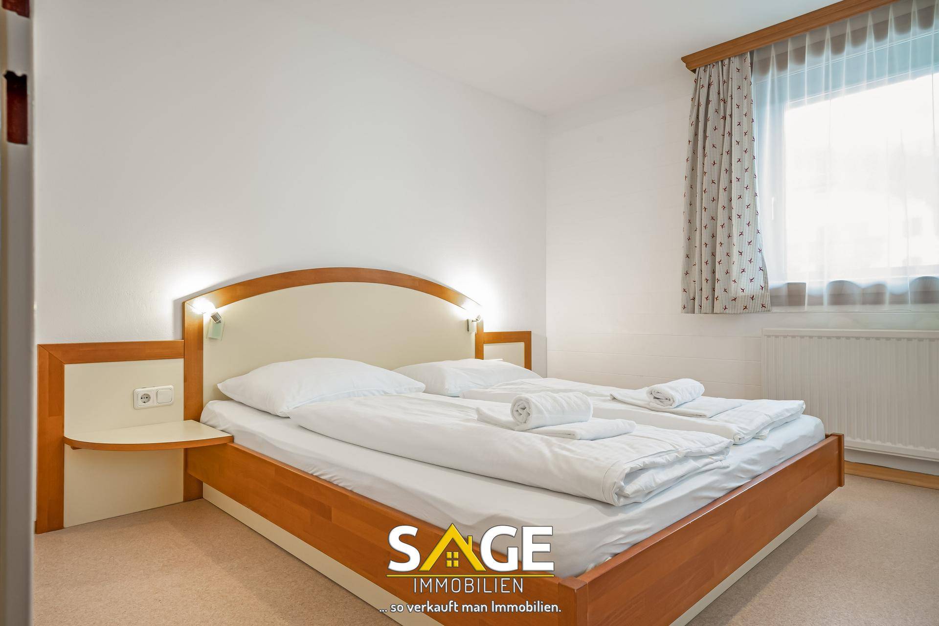 Komfortables Schlafzimmer mit Doppelbett, Nachttischen und einem großen Fenster für natürliches Licht.