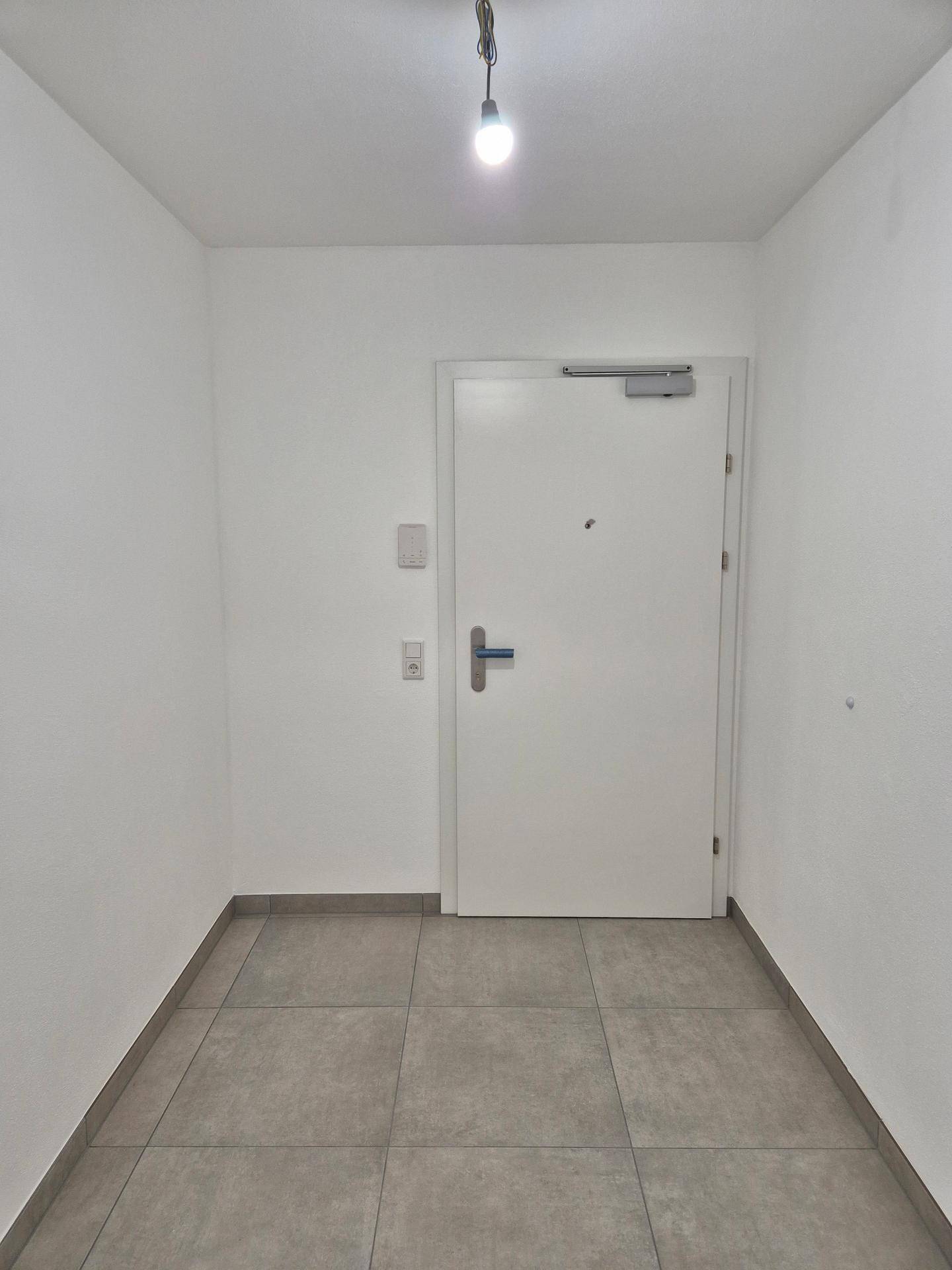 Heller Eingangsbereich mit Fliesenboden und einer modernen Wohnungstür.