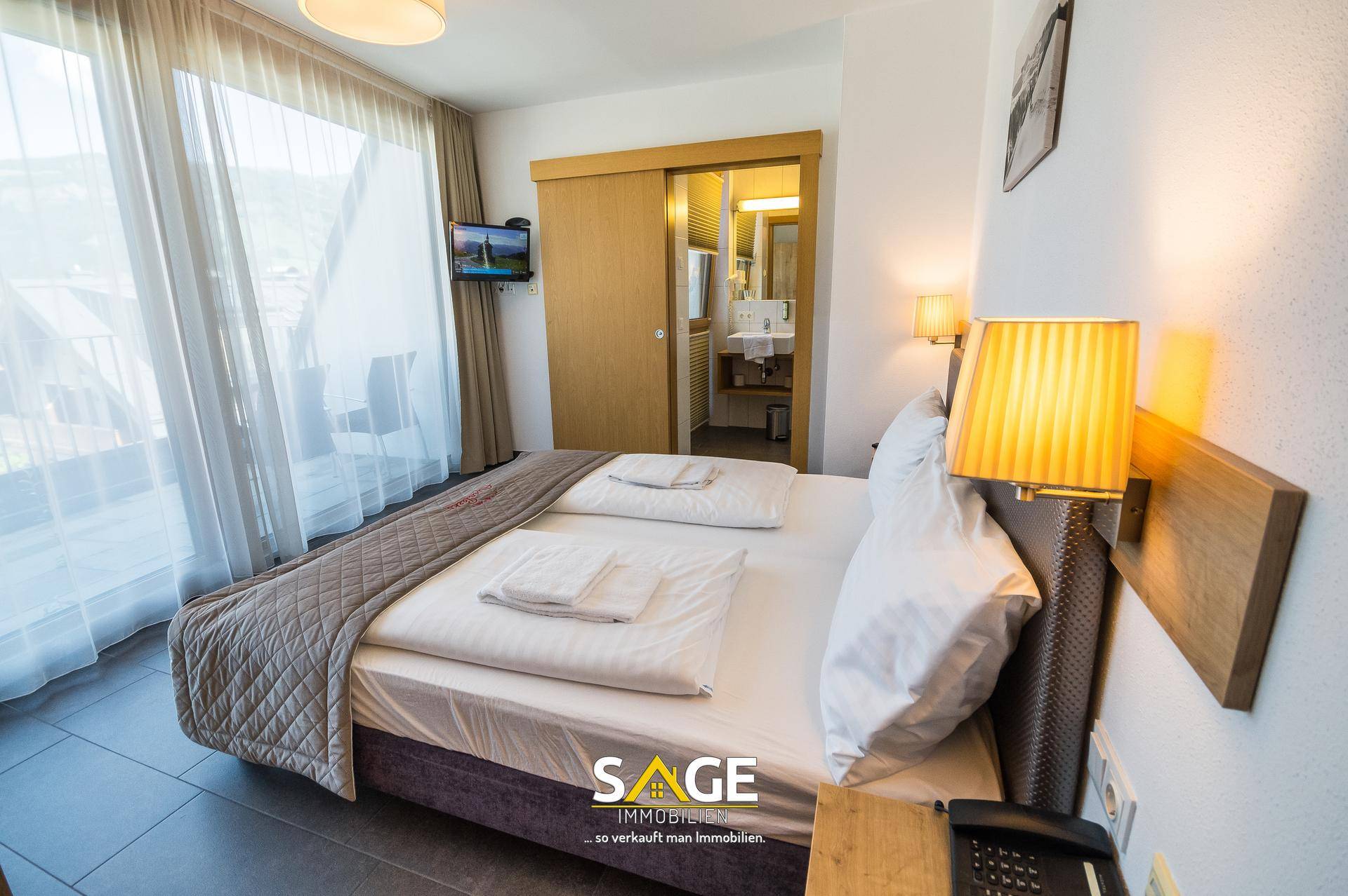 Gemütliches Schlafzimmer mit Doppelbett, Zugang zum Balkon und Blick ins Badezimmer.