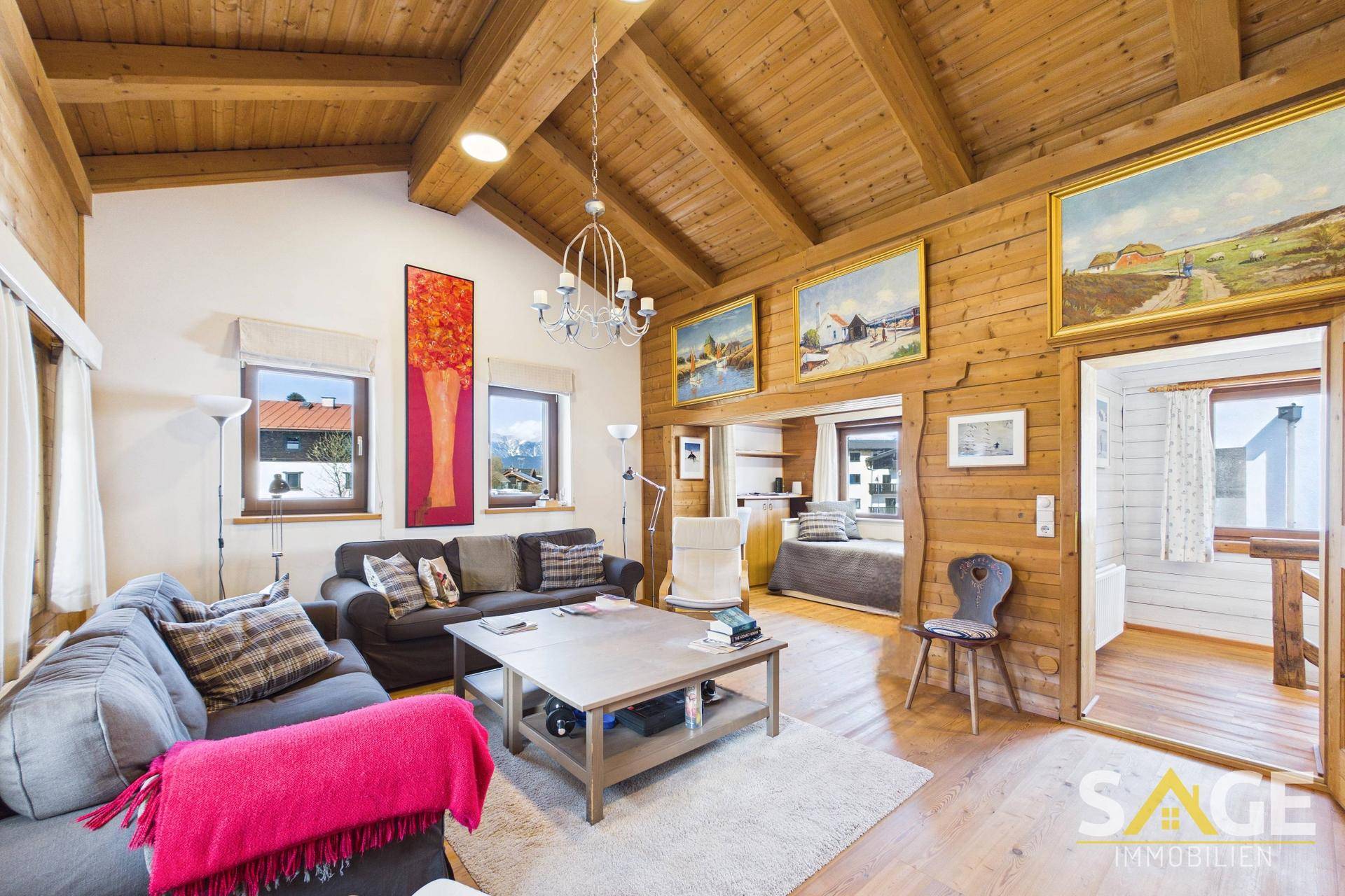 Geräumiges Wohnzimmer im alpinen Stil mit Holzwänden, hohen Decken und Zugang zu einem weiteren Raum.