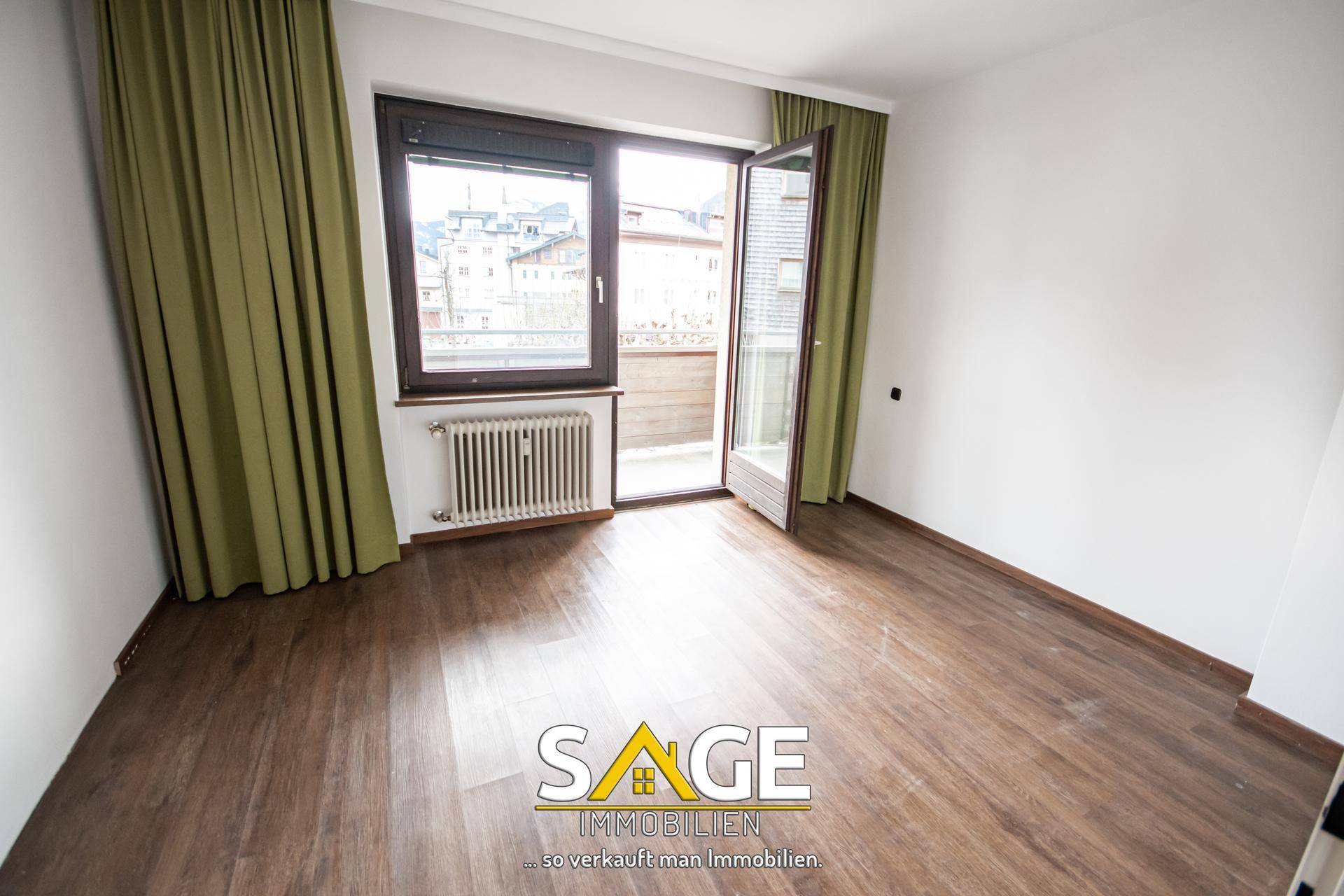 Geräumiger, heller Raum mit Laminatboden, Zugang zum Balkon und einem Heizkörper.