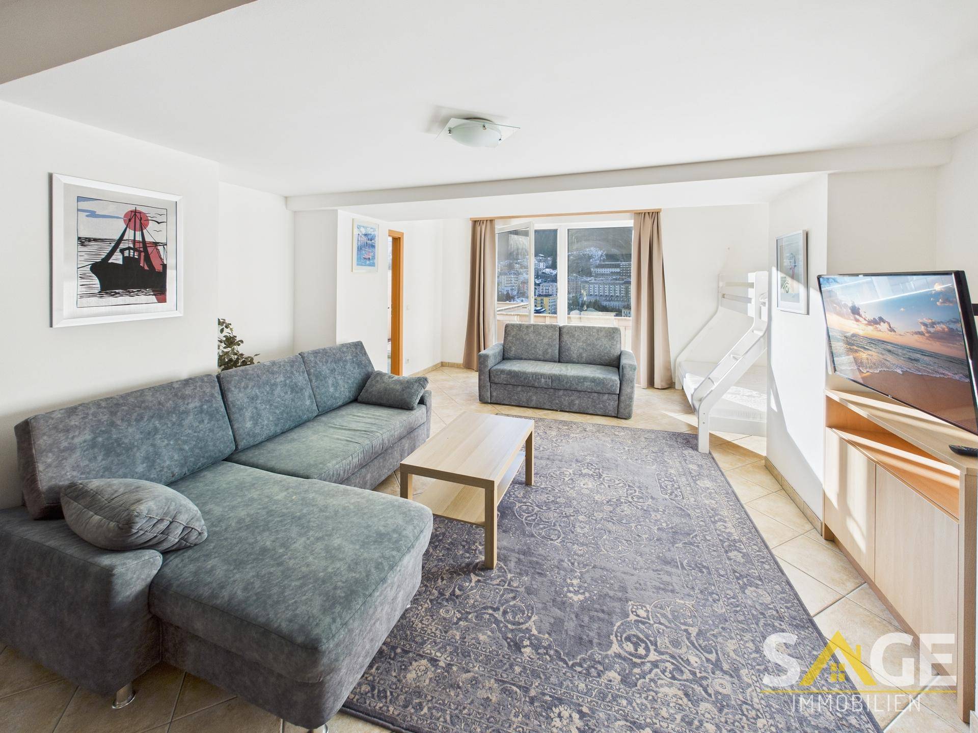 Gemütliches Wohnzimmer mit bequemen Sofas, Teppichboden und Blick auf die verschneite Umgebung.