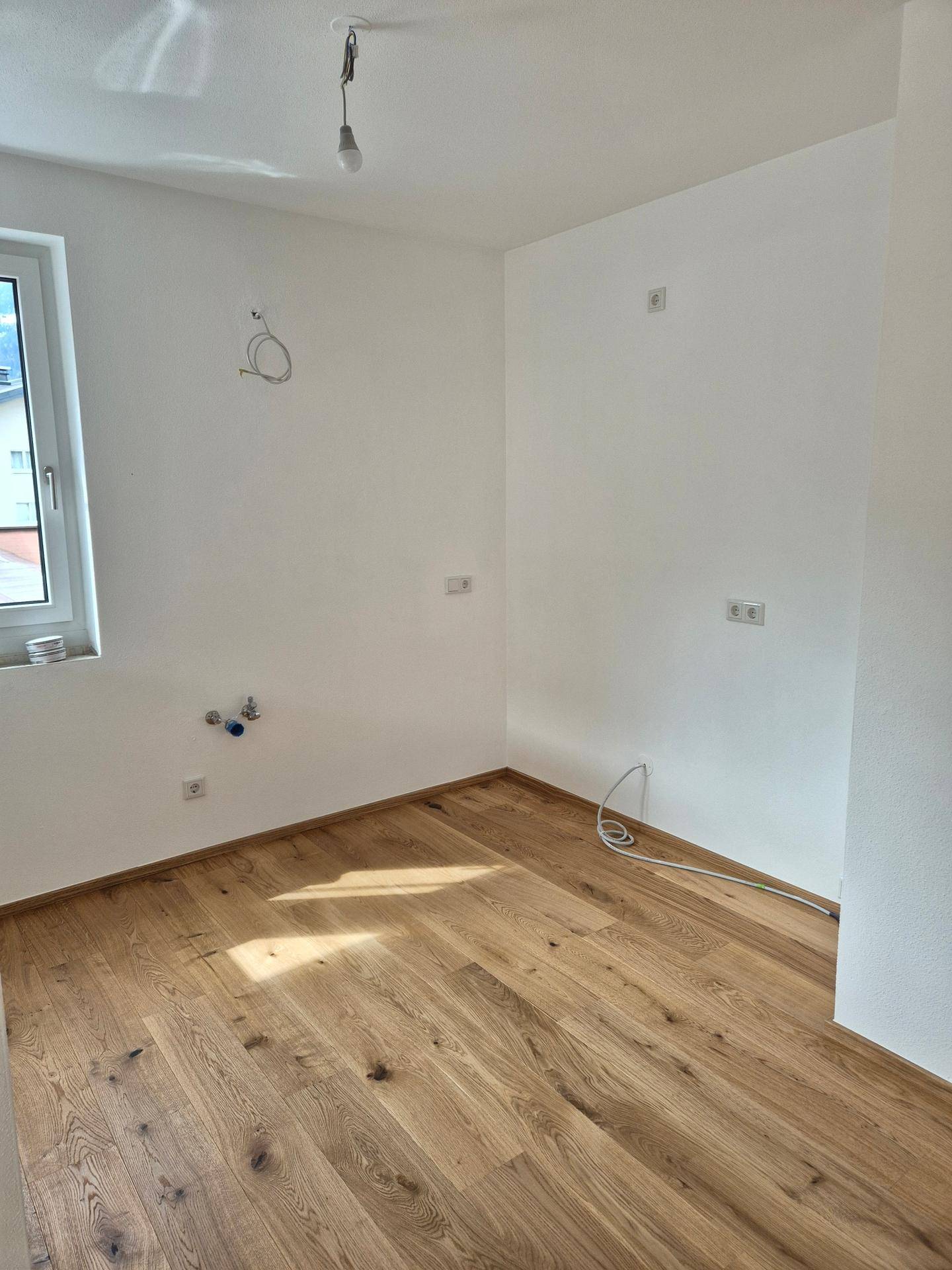 Heller Raum mit Holzboden und Anschlüssen für eine zukünftige Küche.