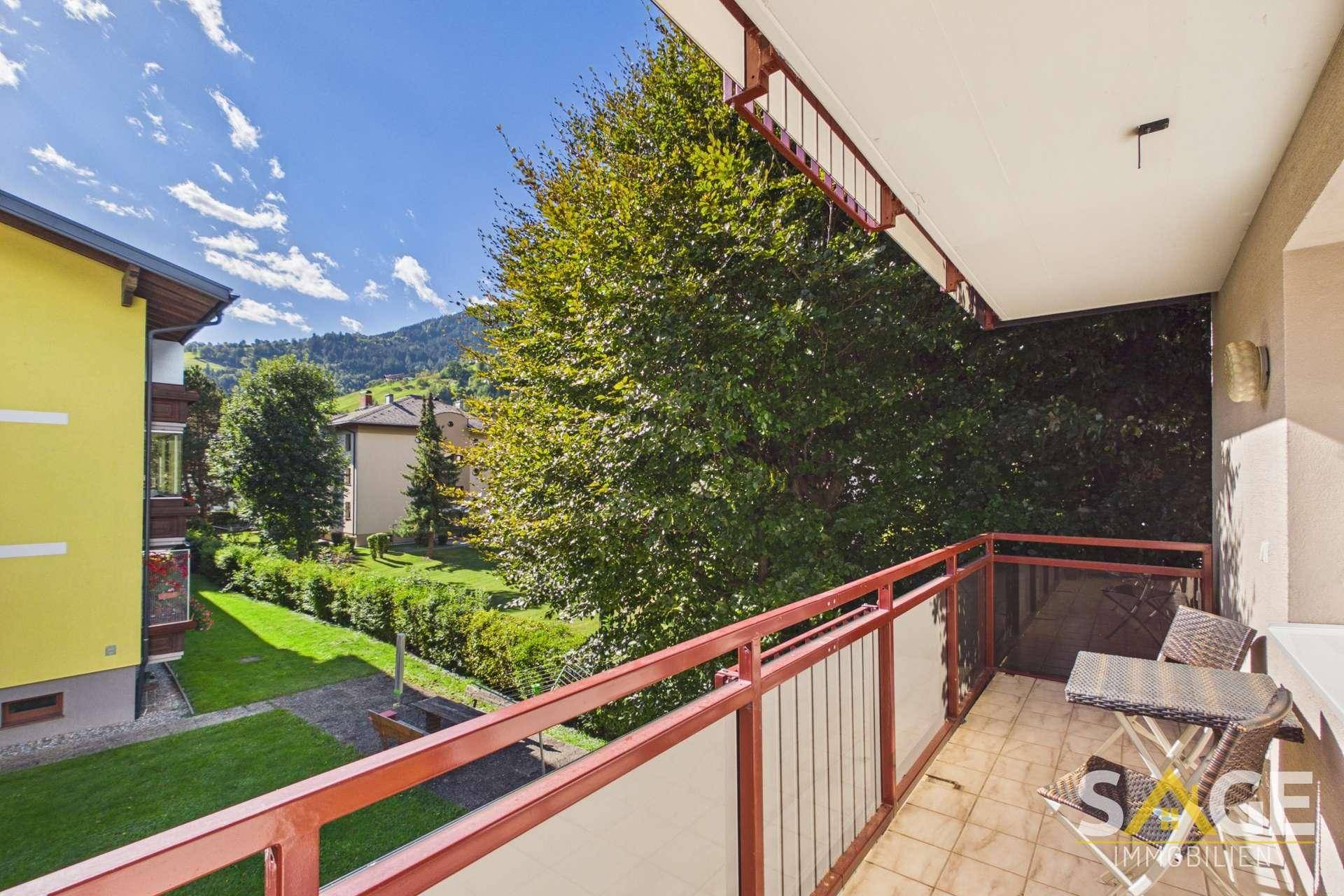 Gemütlicher Balkon mit Fliesenboden, Sitzgelegenheiten und Blick auf die Berge und den Garten.