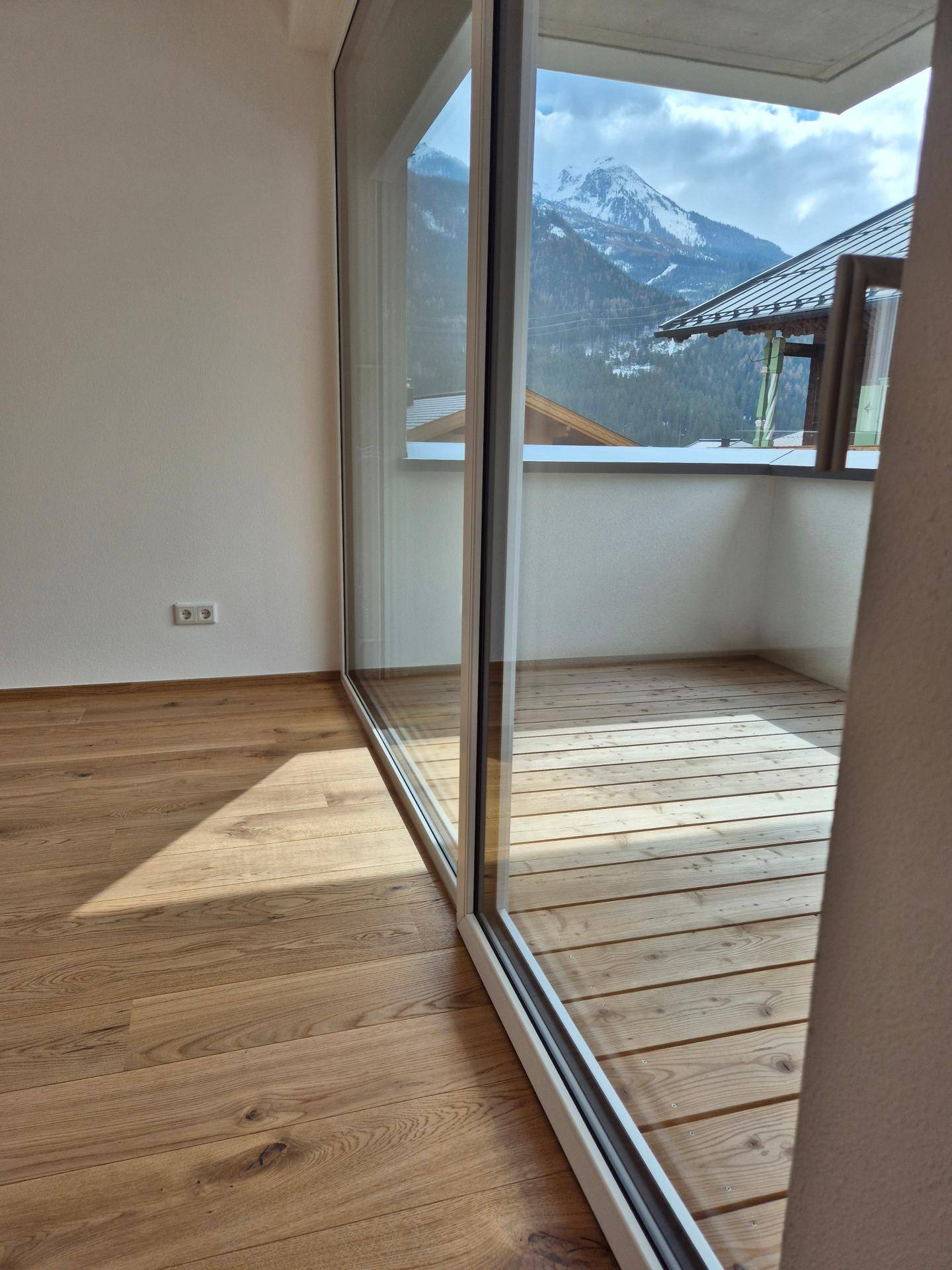 Blick vom Innenraum auf den Balkon mit Holzboden und beeindruckendem Bergblick.