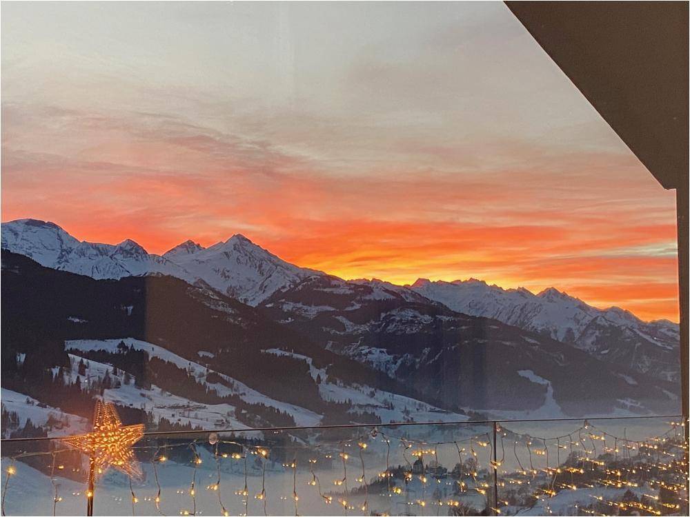 Spektakulärer Sonnenuntergang über den verschneiten Bergen, gesehen von einem Balkon mit festlicher Beleuchtung.