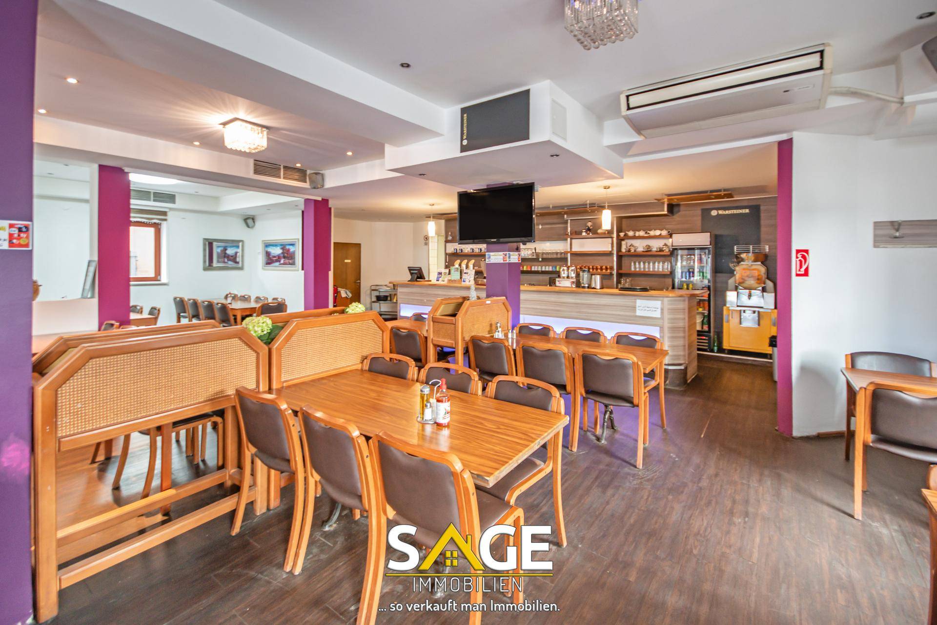 Geräumiger Gastraum mit Holztischen, Stühlen und einer Bar, geeignet für ein Restaurant oder Café.