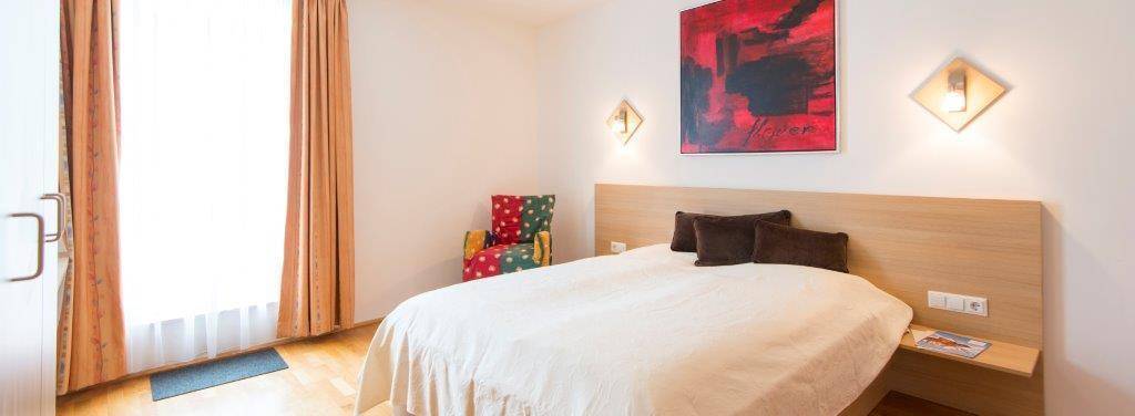 Gemütliches Schlafzimmer mit großem Fenster, Holzboden und farbigen Akzenten.