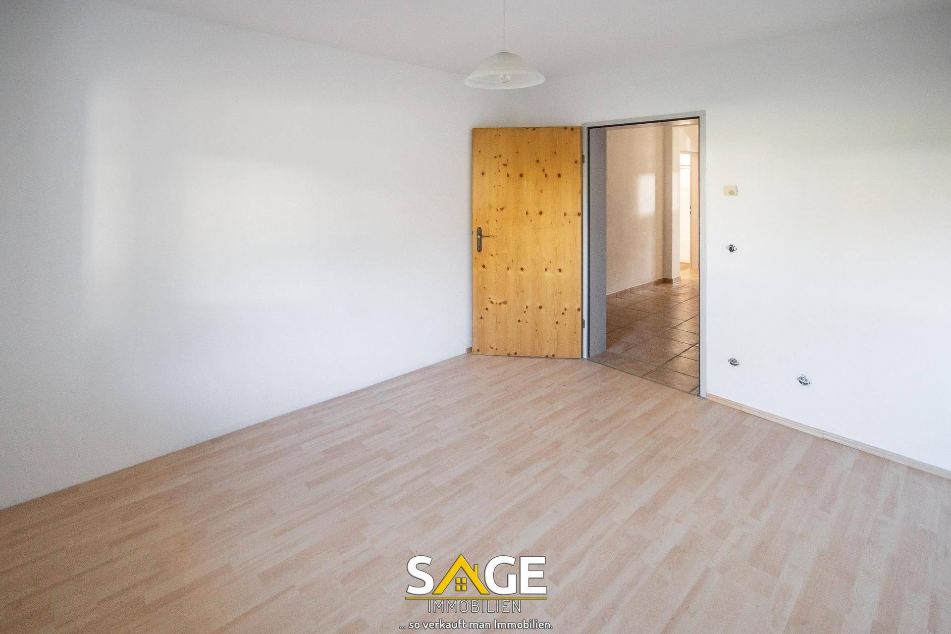 Leeres Zimmer mit hellem Laminatboden und weiß gestrichenen Wänden.