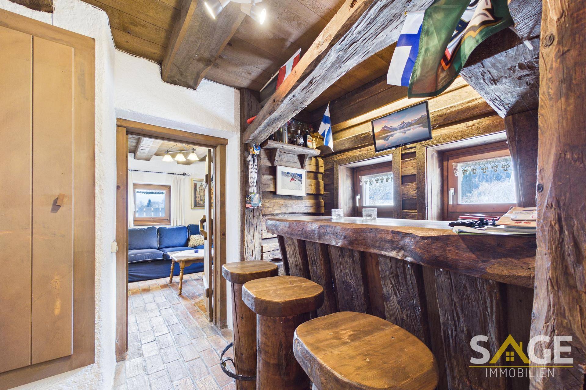 Rustikale Hausbar mit Holzelementen, Barhockern und Blick in den Wohnbereich.