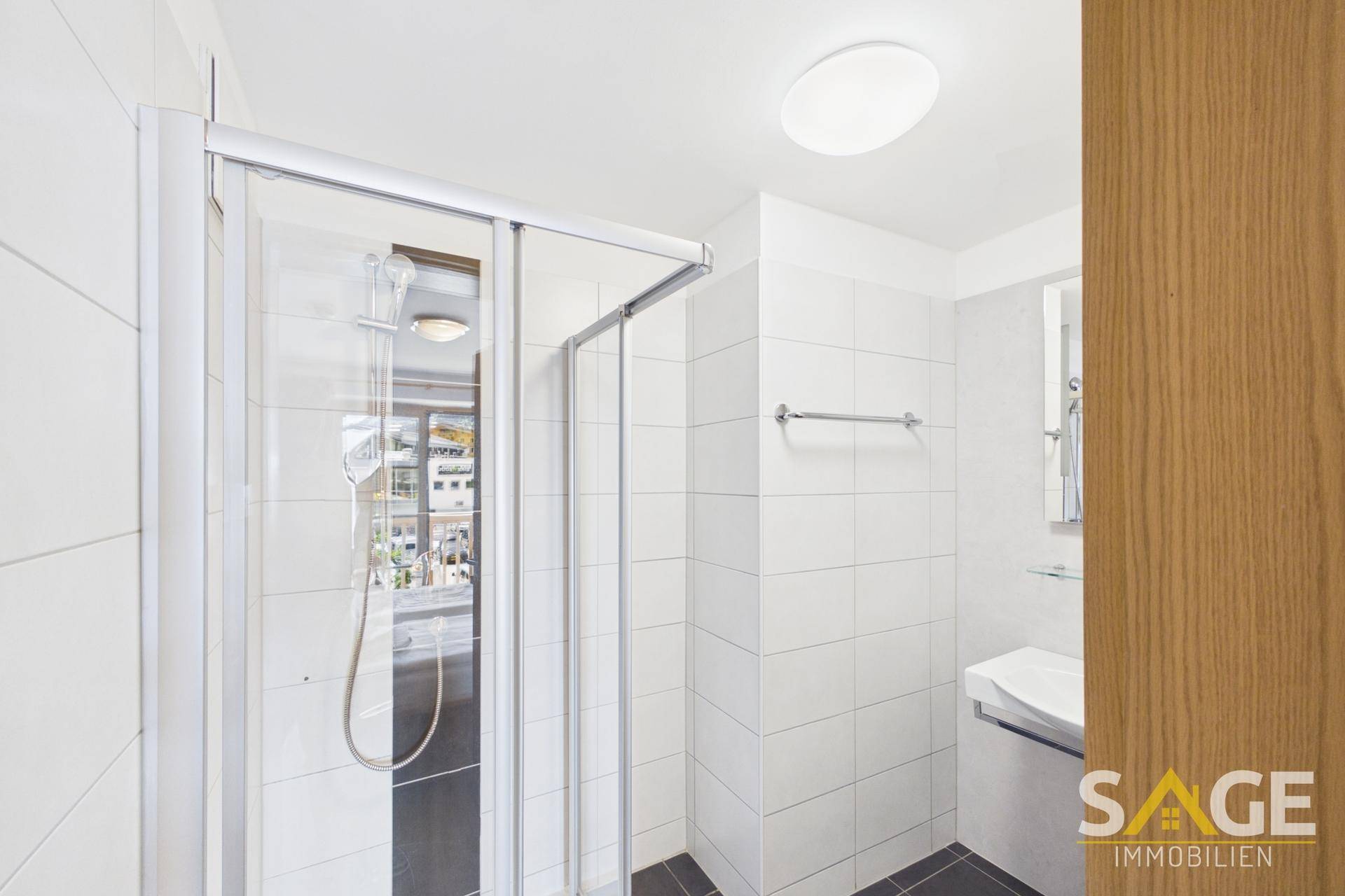 Modernes Badezimmer mit Duschkabine, weißen Fliesen und einem Waschbecken.