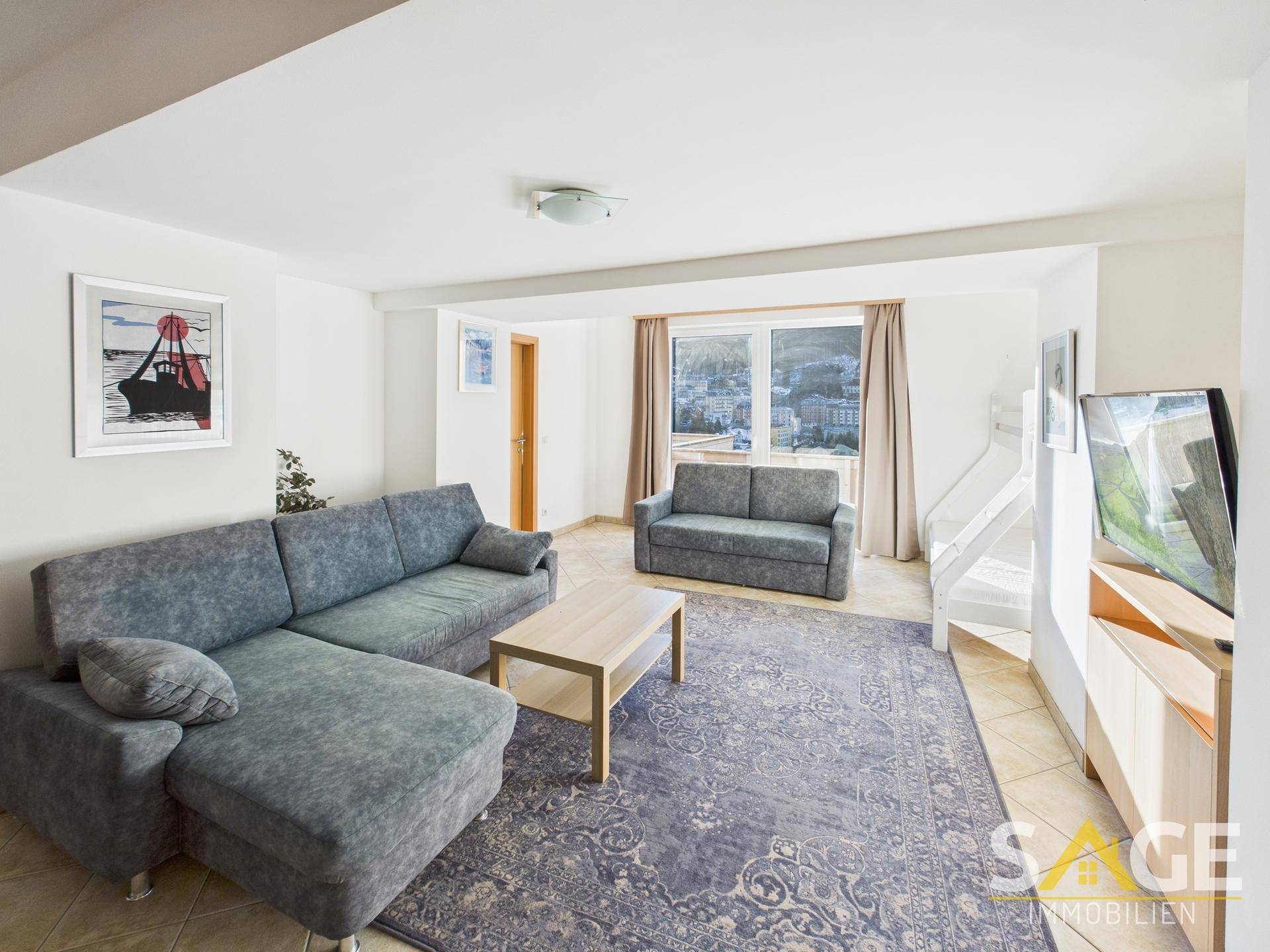 Geräumiges Wohnzimmer mit bequemen Sofas, Teppich und Blick auf die verschneite Berglandschaft.