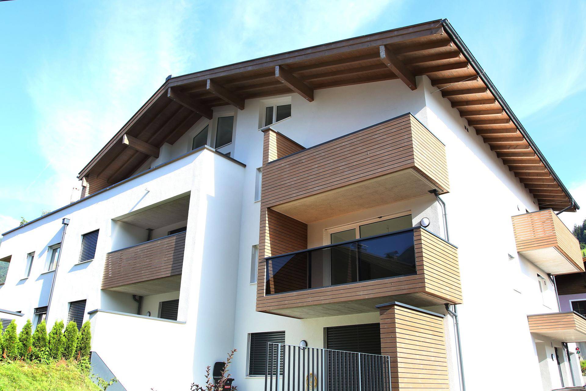 Moderne Wohnanlage mit weißer Fassade, Holzverkleidung und mehreren Balkonen.