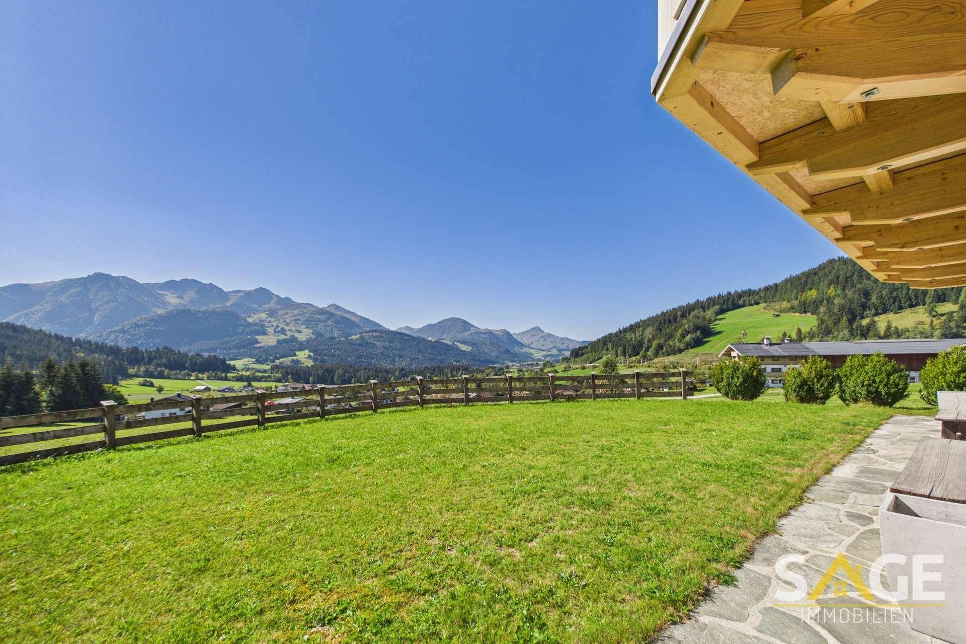 Großer grüner Gartenbereich mit Holzzaun und Panoramablick auf die umliegende Berglandschaft.