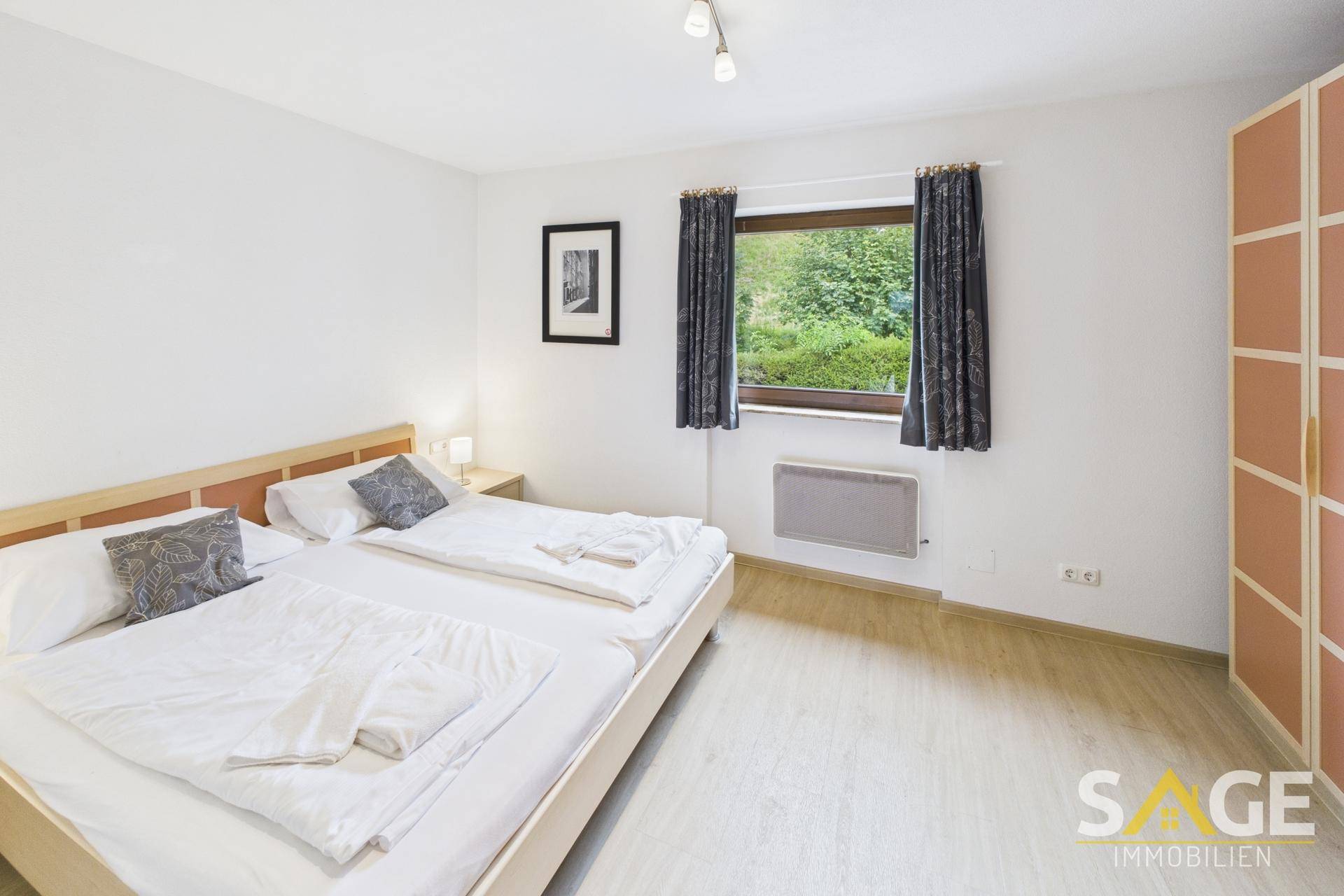 Helles Schlafzimmer mit zwei Einzelbetten, Laminatboden und Blick ins Grüne.