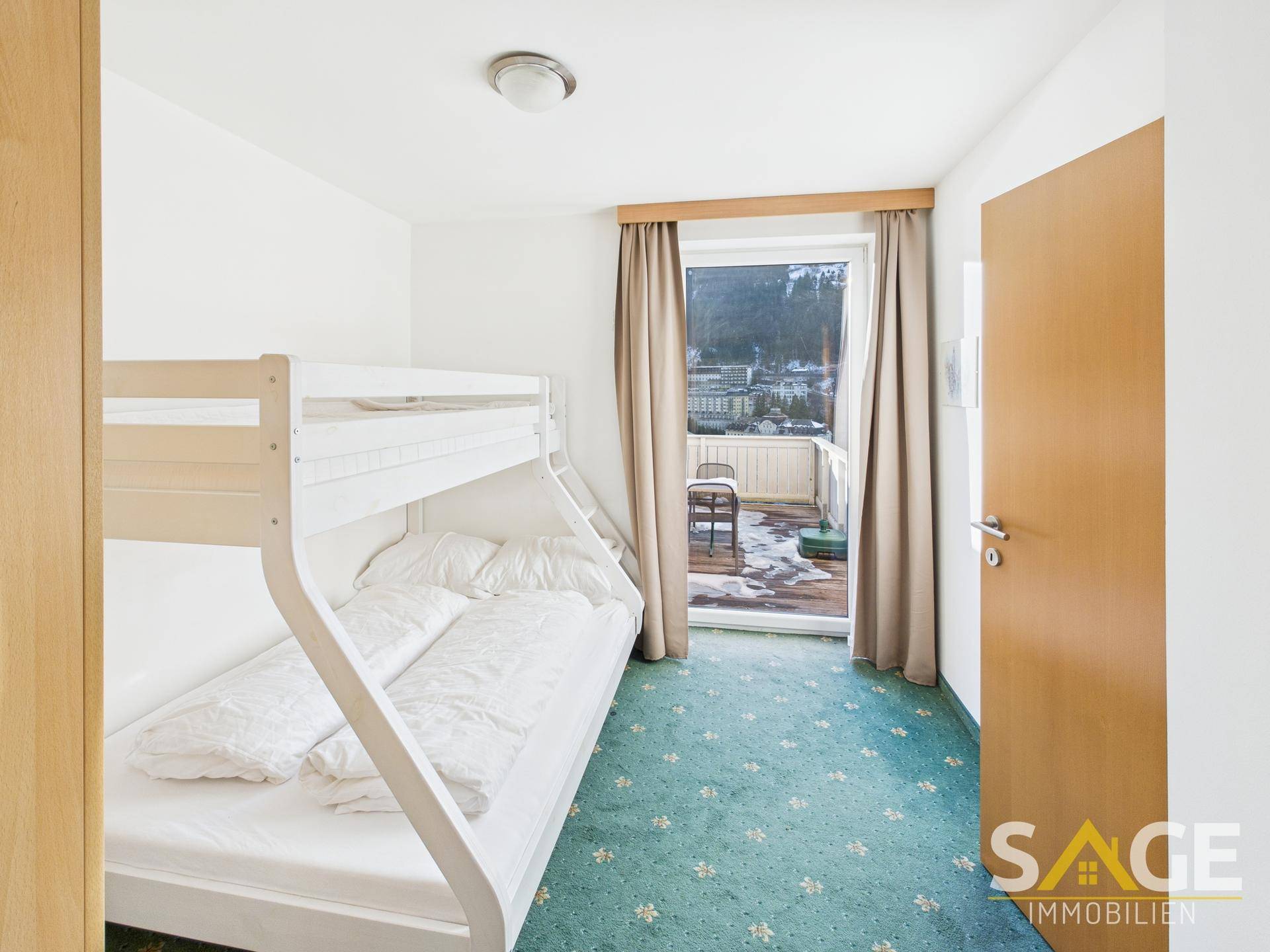 Schlafzimmer mit Etagenbett, Teppichboden und Zugang zu einem kleinen Balkon mit Bergblick.
