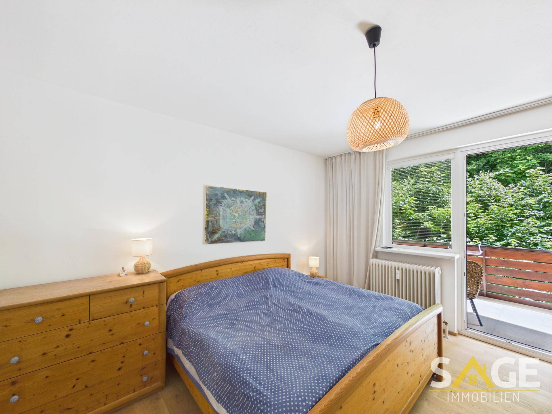 Gemütliches Schlafzimmer mit Holzbett, Kommode und direktem Zugang zum Balkon mit Grünblick.