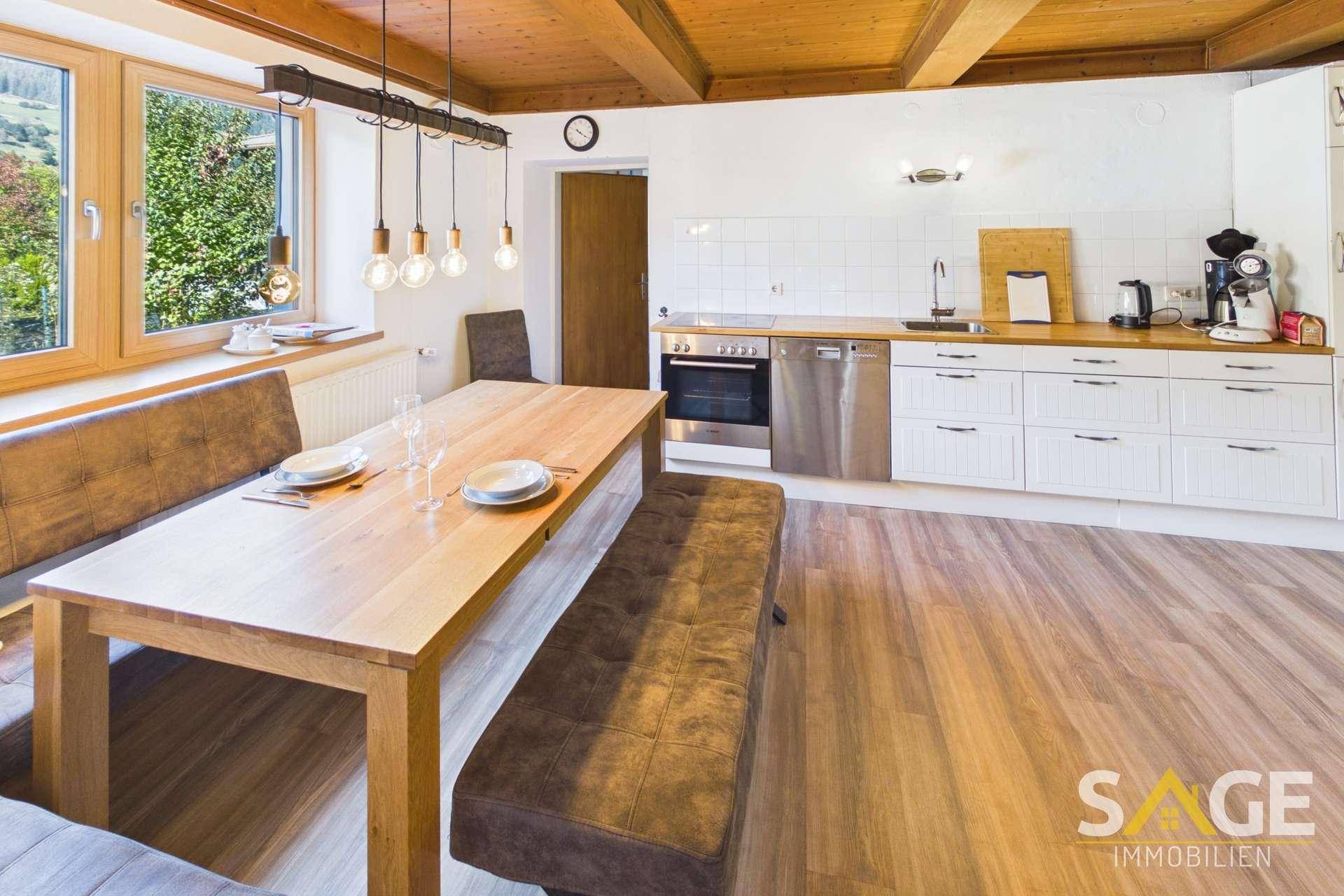 Rustikale Wohnküche mit Holzbalkendecke, Esstisch und modernen Einbaugeräten.