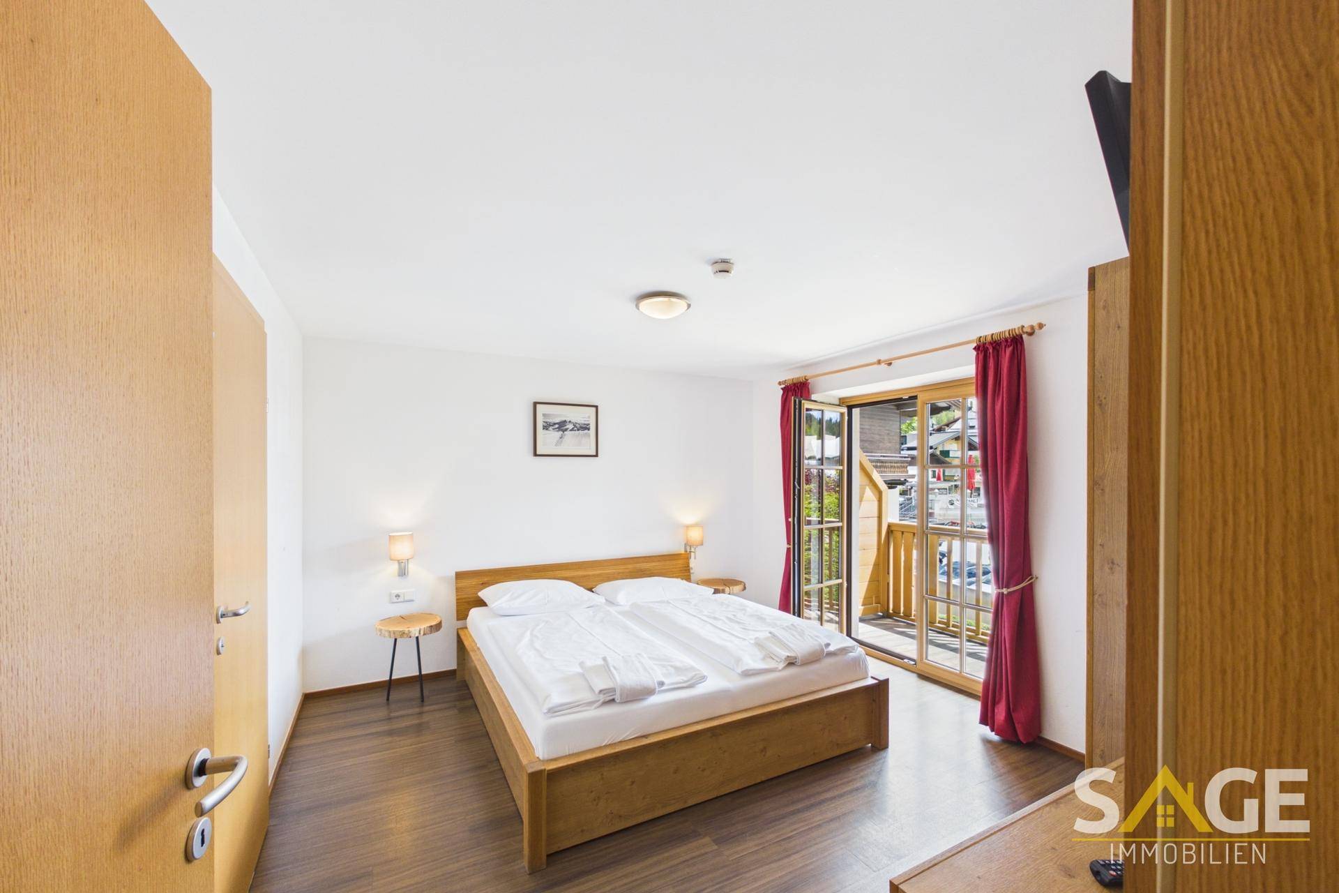 Helles Schlafzimmer mit Holzbett, Nachttischen und Zugang zu einem Balkon.