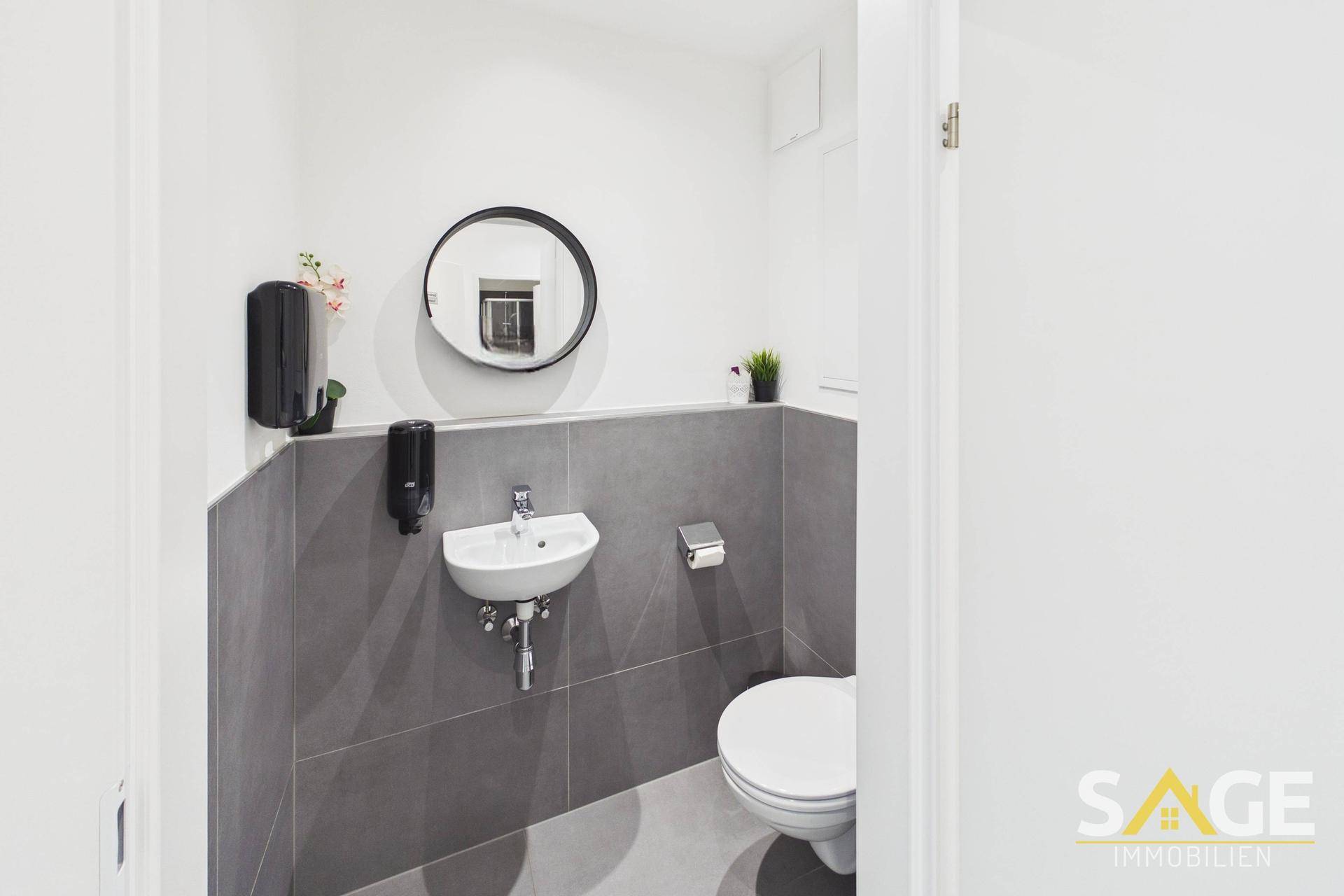 Kleines, modernes Gäste-WC mit Wand-WC, kleinem Waschbecken und rundem Spiegel.
