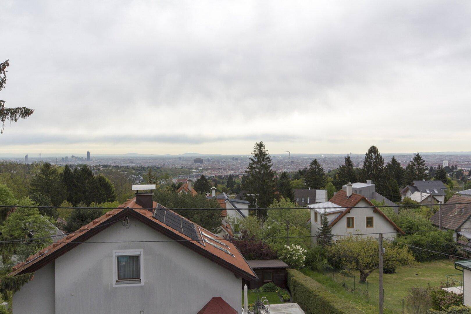 Weitläufiger Blick über die Stadt und die umliegende grüne Landschaft unter bewölktem Himmel.