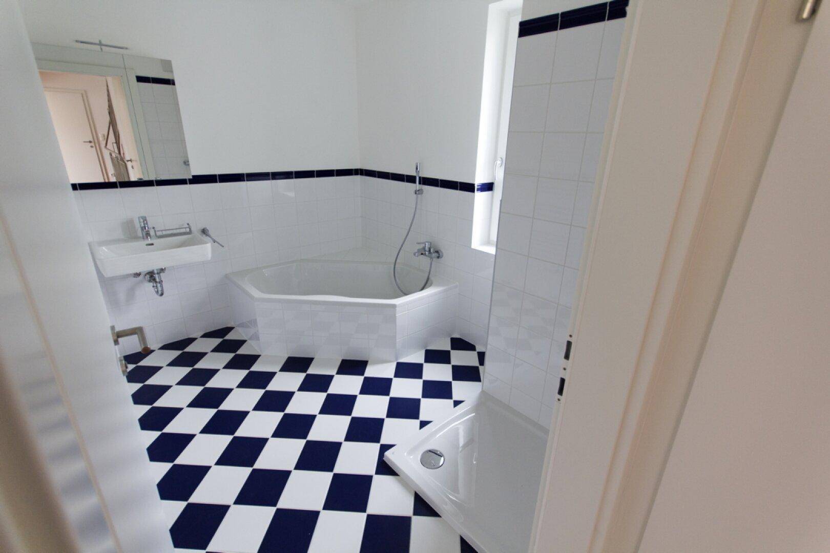 Badezimmer mit kariertem Fliesenboden, Eckbadewanne, Dusche und Fenster.