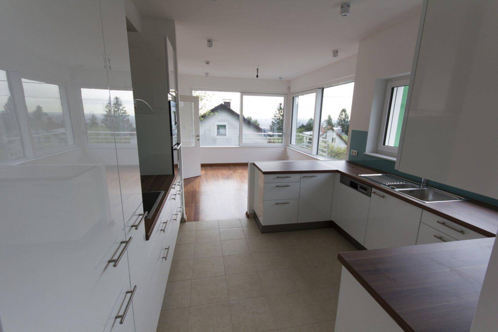 Moderne Küche mit weißen Hochglanzfronten, Fliesenboden und weitem Ausblick über die Landschaft.
