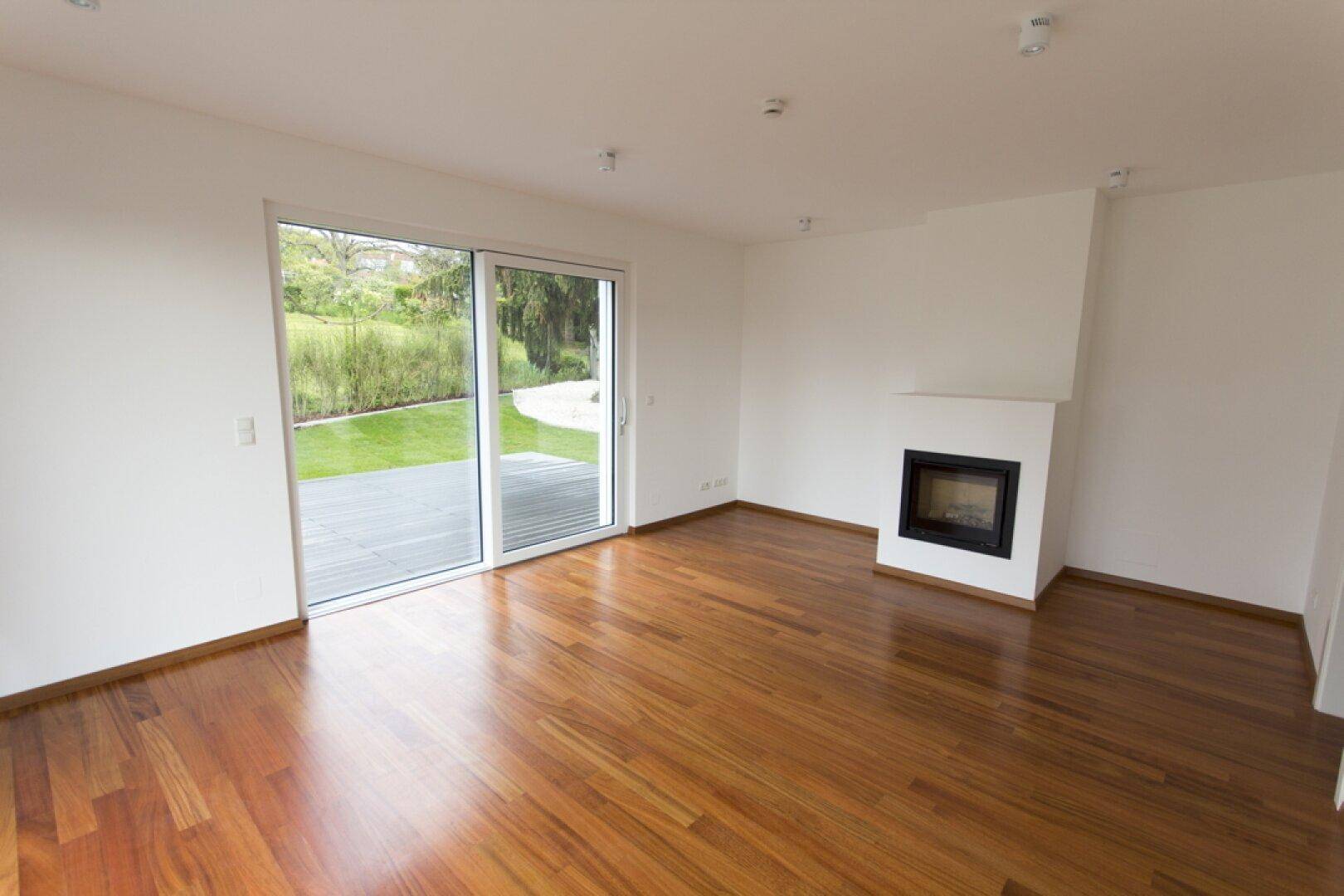 Geräumiges Wohnzimmer mit Holzboden, Kamin und Zugang zur Terrasse und Garten.