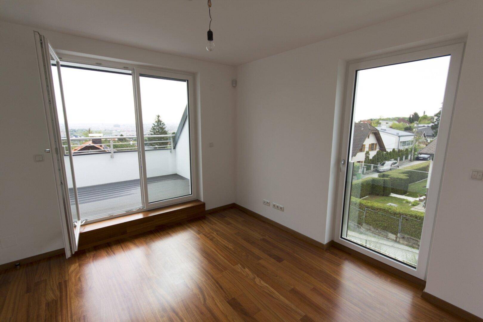 Helles Zimmer mit Holzboden, Balkonzugang und Blick auf die Umgebung.