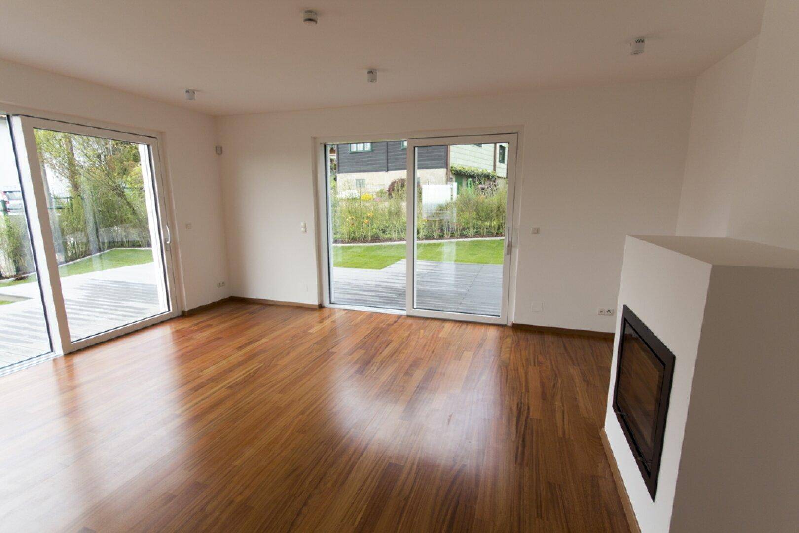 Helles Wohnzimmer mit Holzboden, Kamin und großen Schiebetüren zum Gartenbereich.