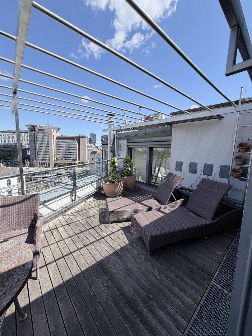 Große Dachterrasse mit Holzdeck, Liegestühlen und Blick auf die Stadt.