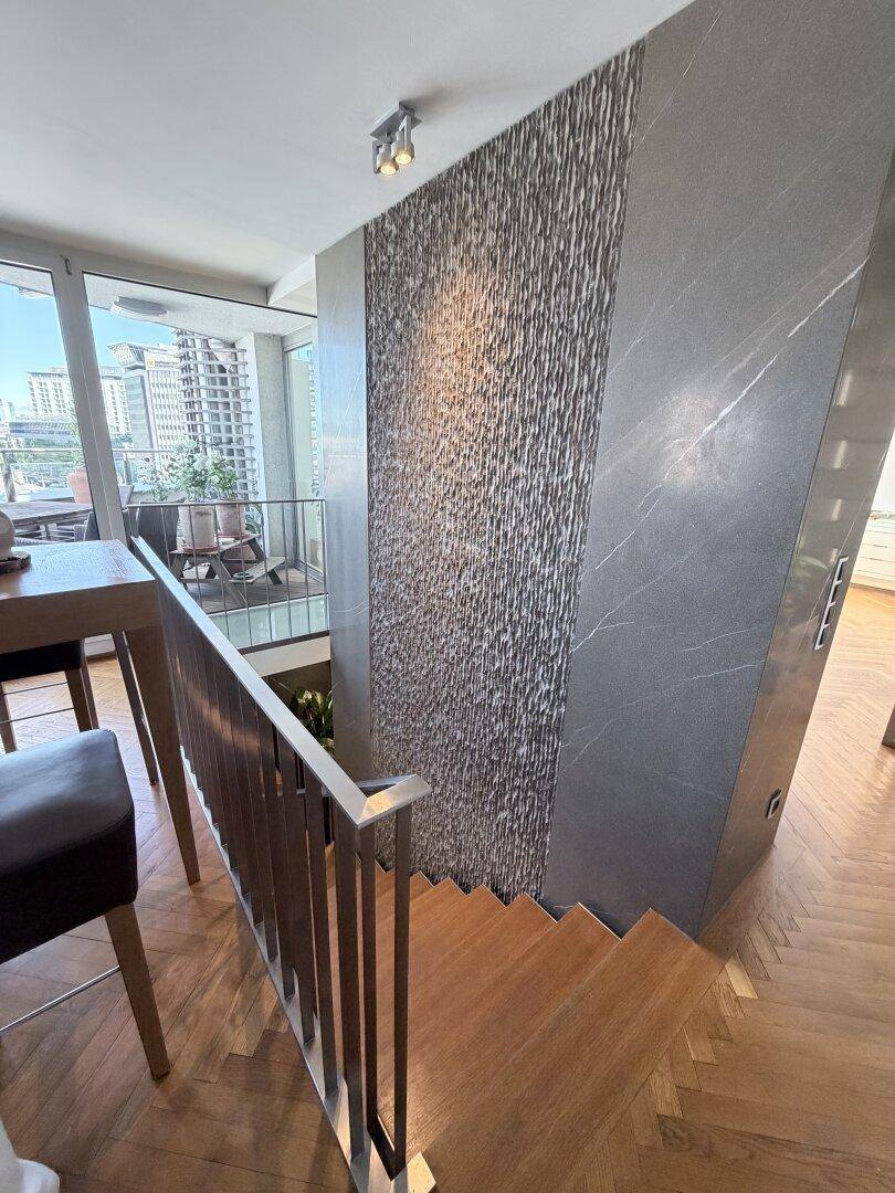 Treppenaufgang mit Holzstufen und moderner Wandverkleidung aus Stein und Marmor.