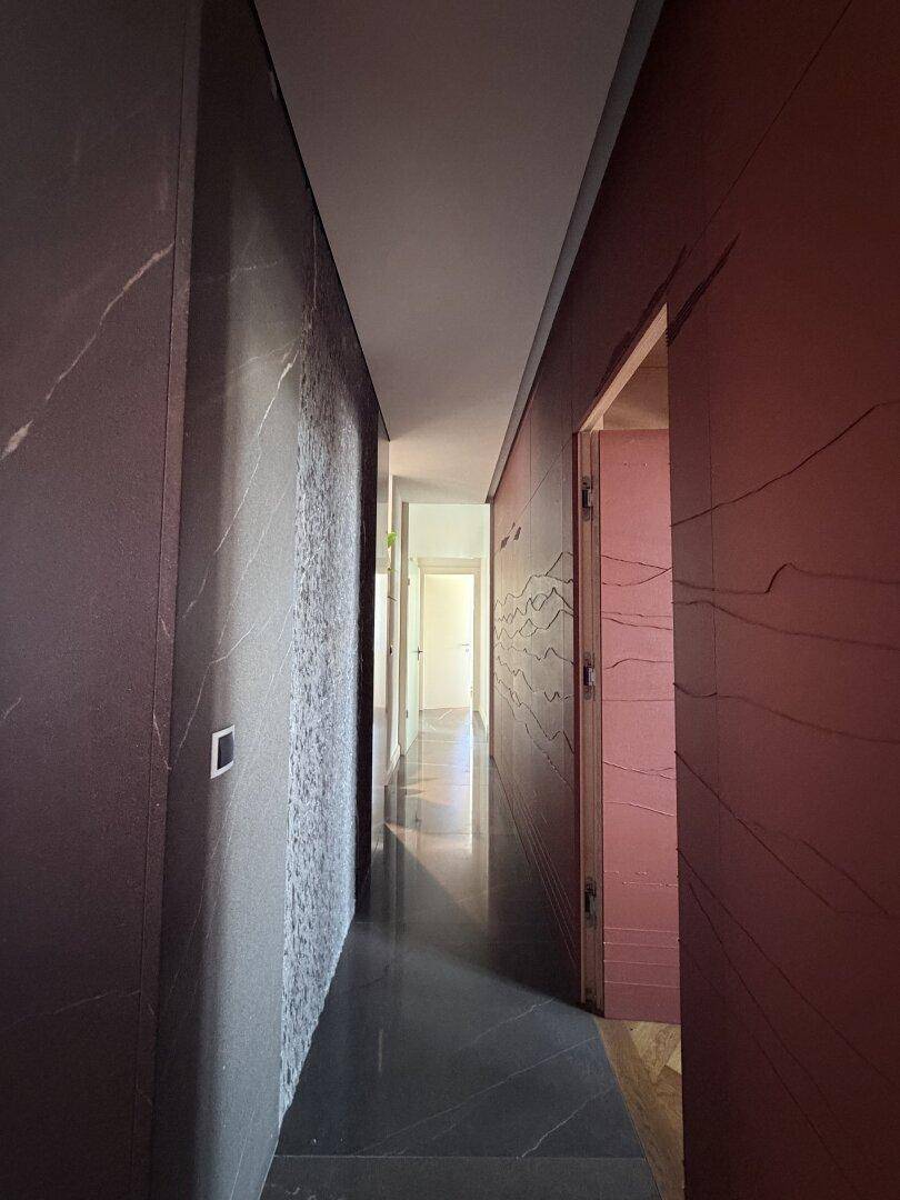 Langer Flur mit dunklem Fliesenboden und dekorativen Wandverkleidungen.