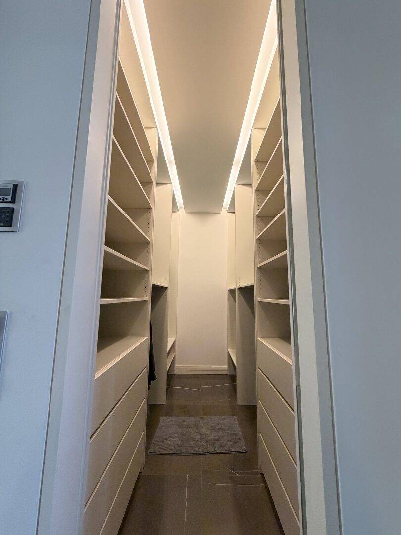 Geräumiger begehbarer Kleiderschrank mit vielen Regalen und integrierter Beleuchtung.