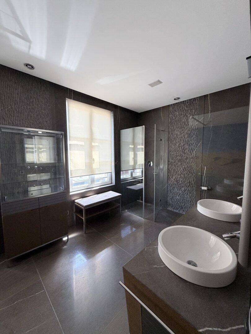 Modernes Badezimmer mit Doppelwaschbecken, großer Dusche und dunklen Fliesen.