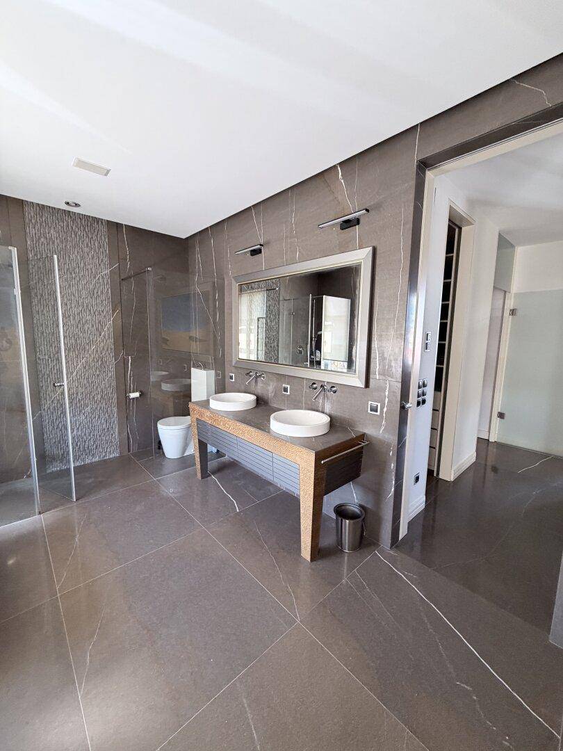 Geräumiges Badezimmer mit Doppelwaschbecken, Dusche und dunklen Marmorfliesen.